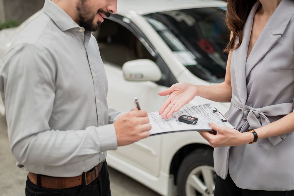 A man is signing a document next to a woman holding a car key .