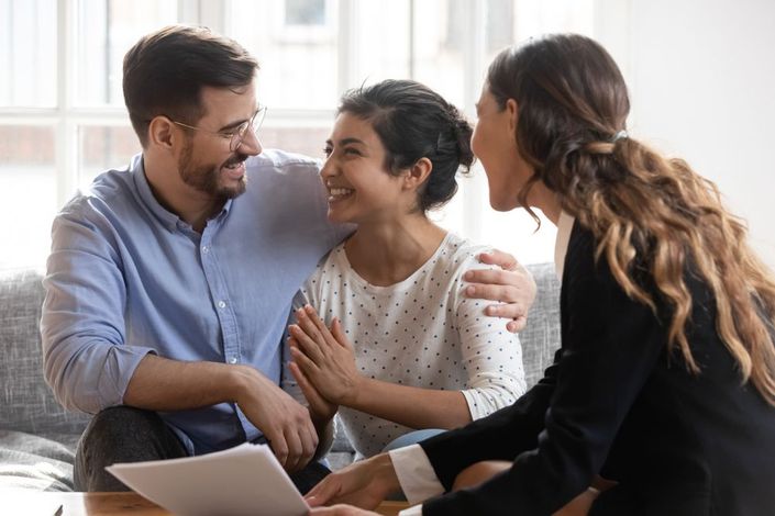 A man and a woman are sitting on a couch talking to a real estate agent .