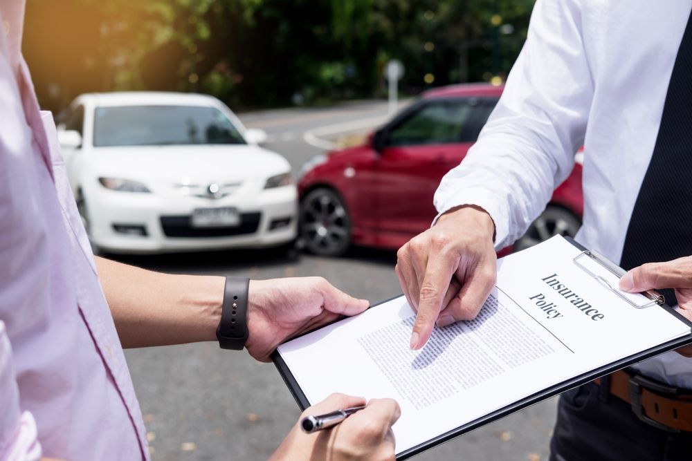 A man is holding a clipboard in front of a car accident .