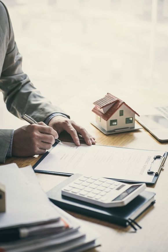 A man is sitting at a desk with a model house and a calculator .