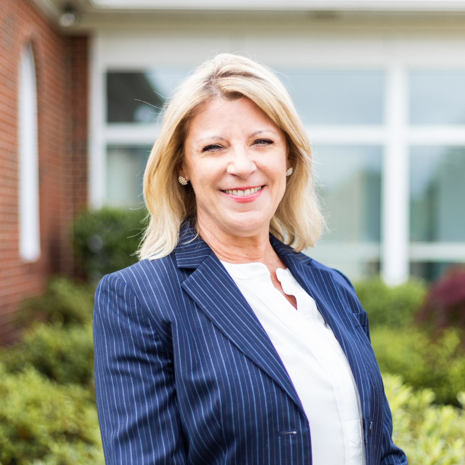 Smiling woman in a navy pinstripe blazer standing outdoors in front of a building