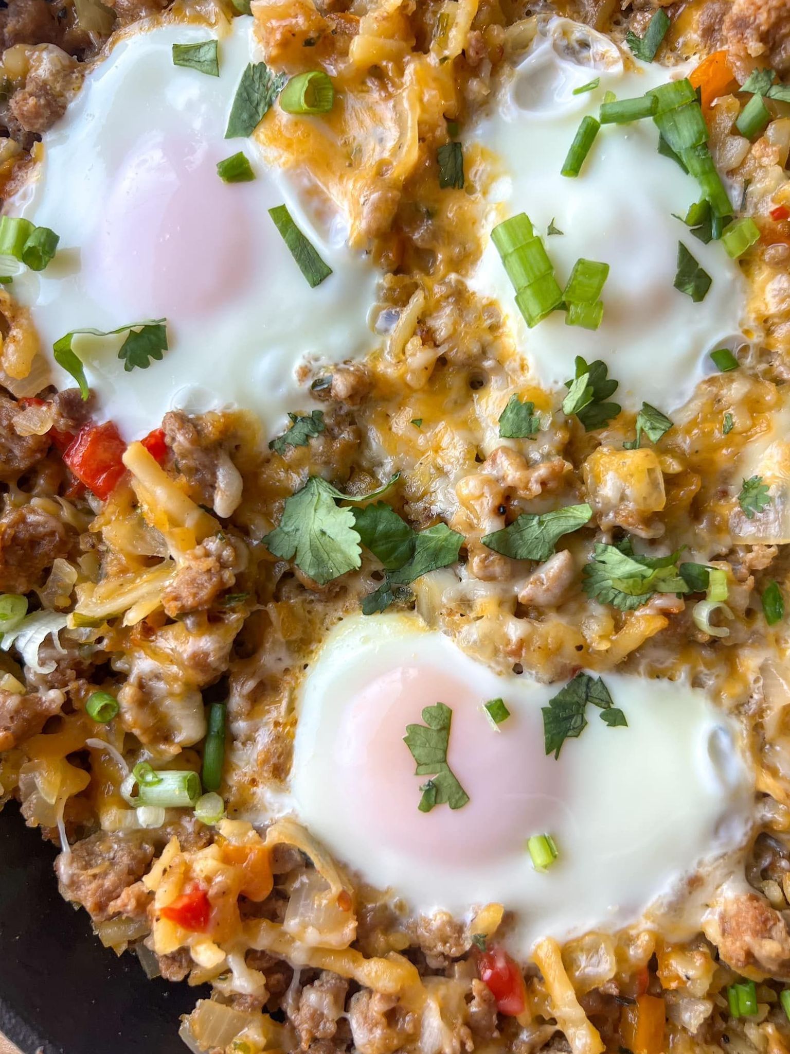 A close up of a skillet filled with eggs , meat , cheese and vegetables.