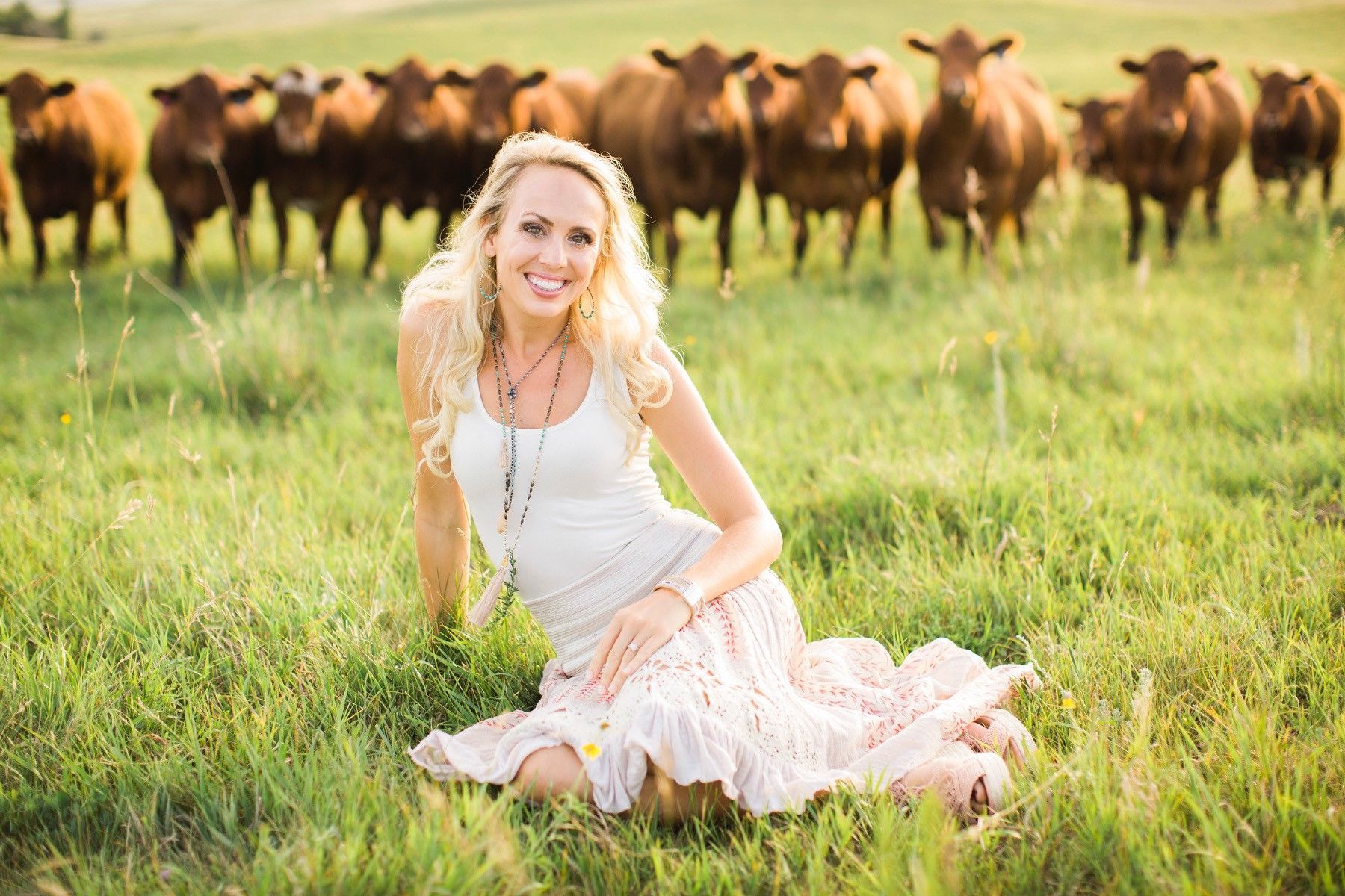 A woman is kneeling in the grass in front of a herd of cows.
