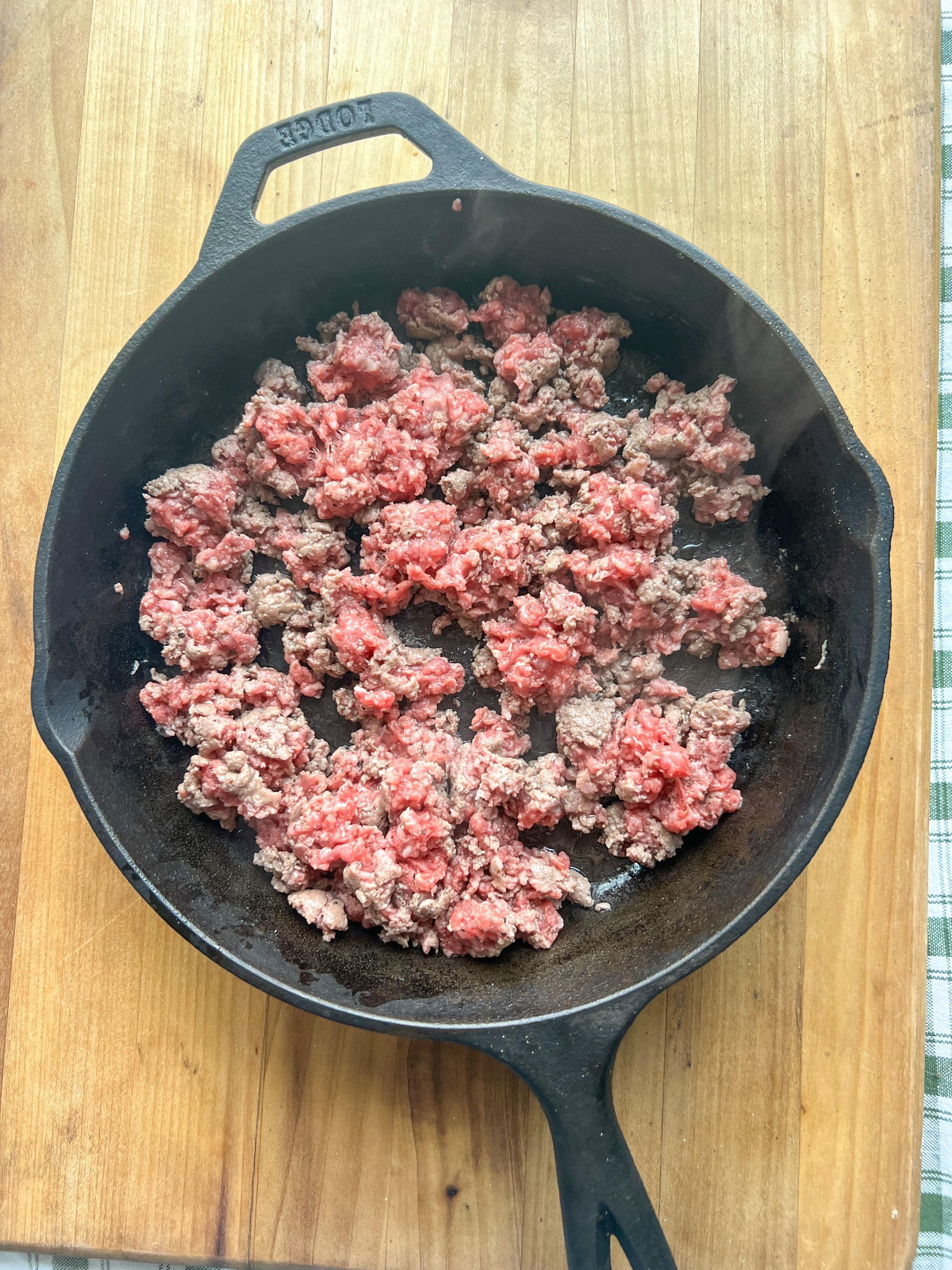 A skillet filled with ground beef is sitting on a wooden table.