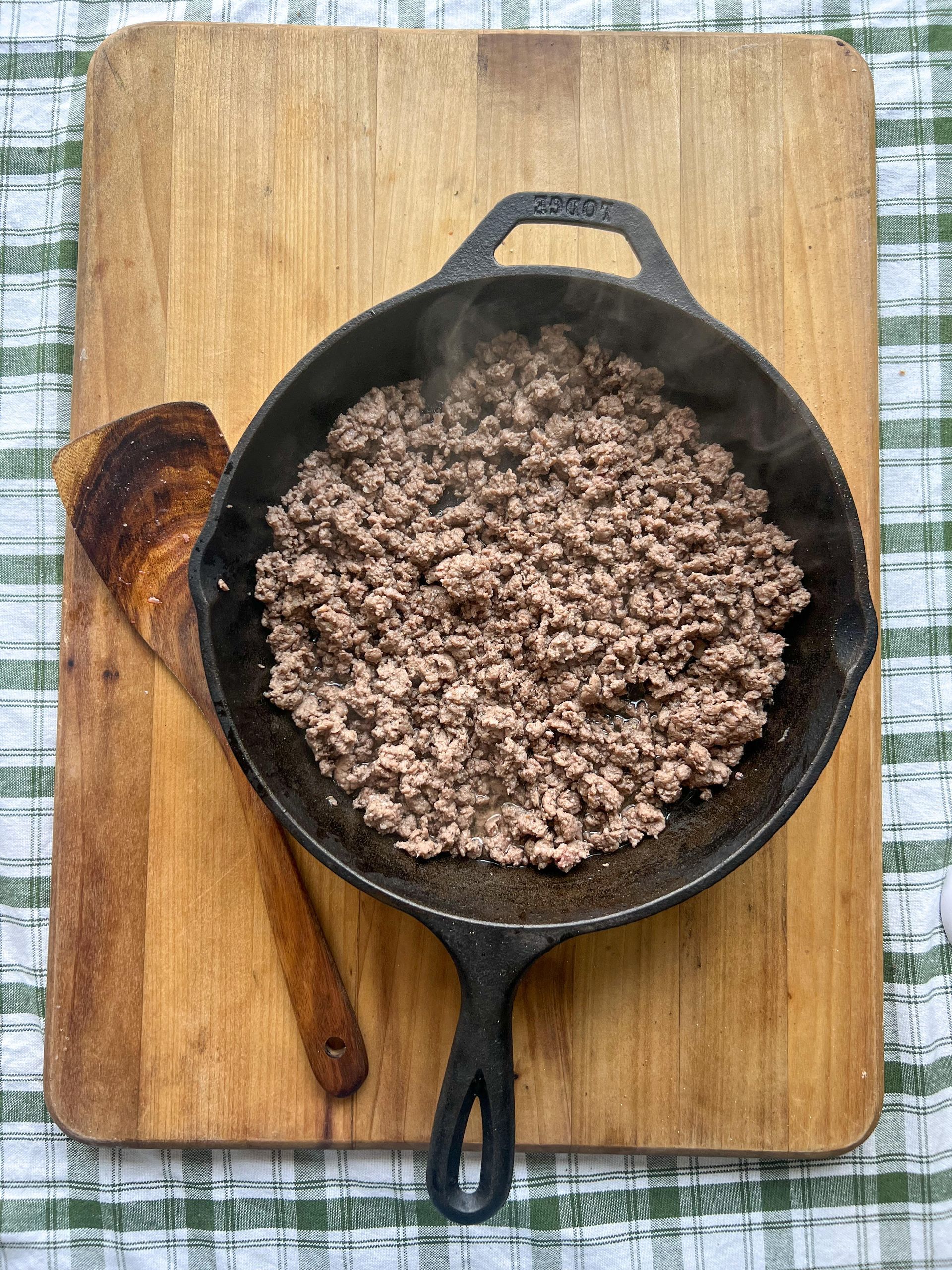 A skillet filled with ground beef is sitting on a wooden cutting board.
