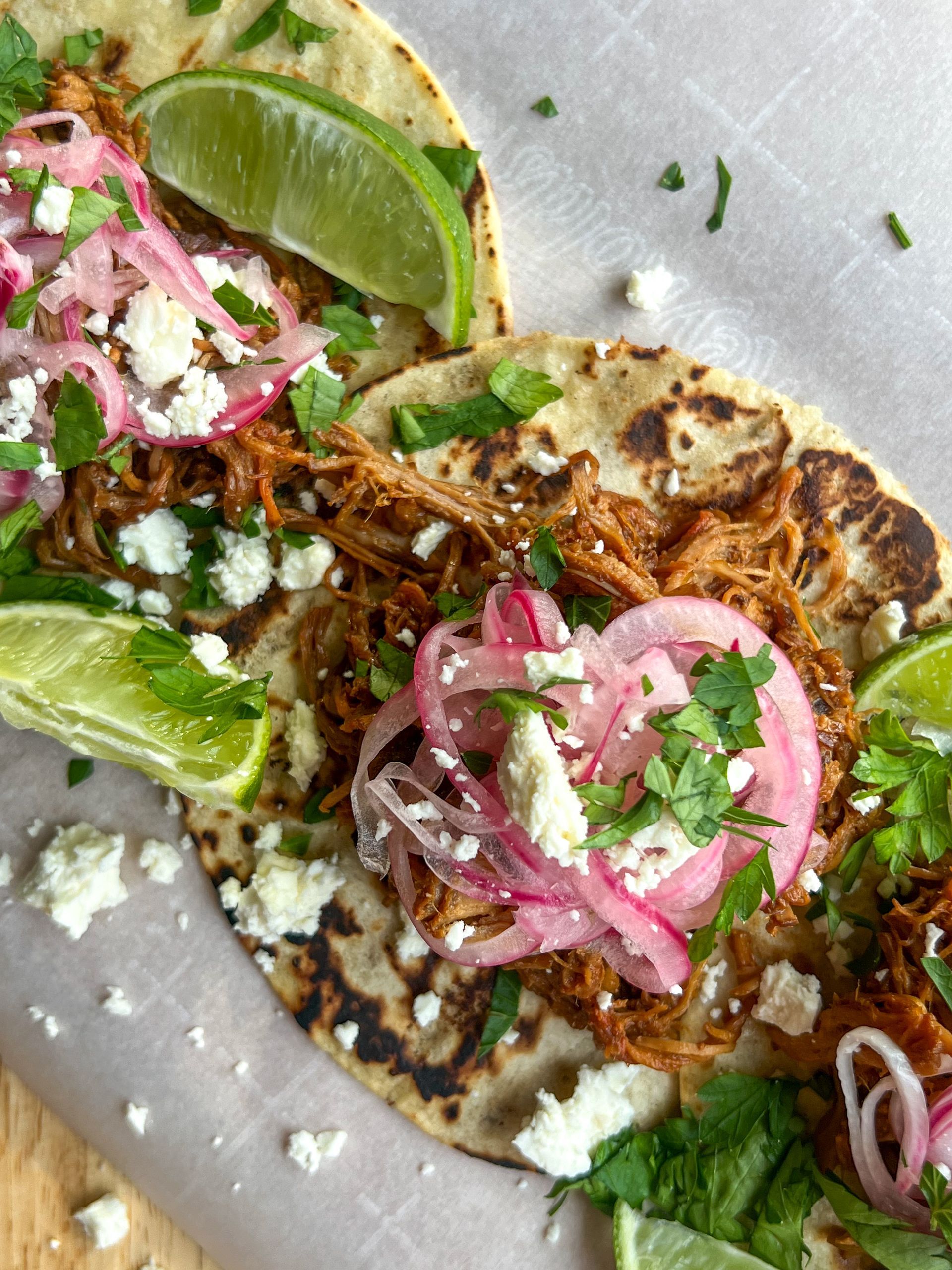 A close up of two tacos with meat , onions , limes and cheese on a plate.
