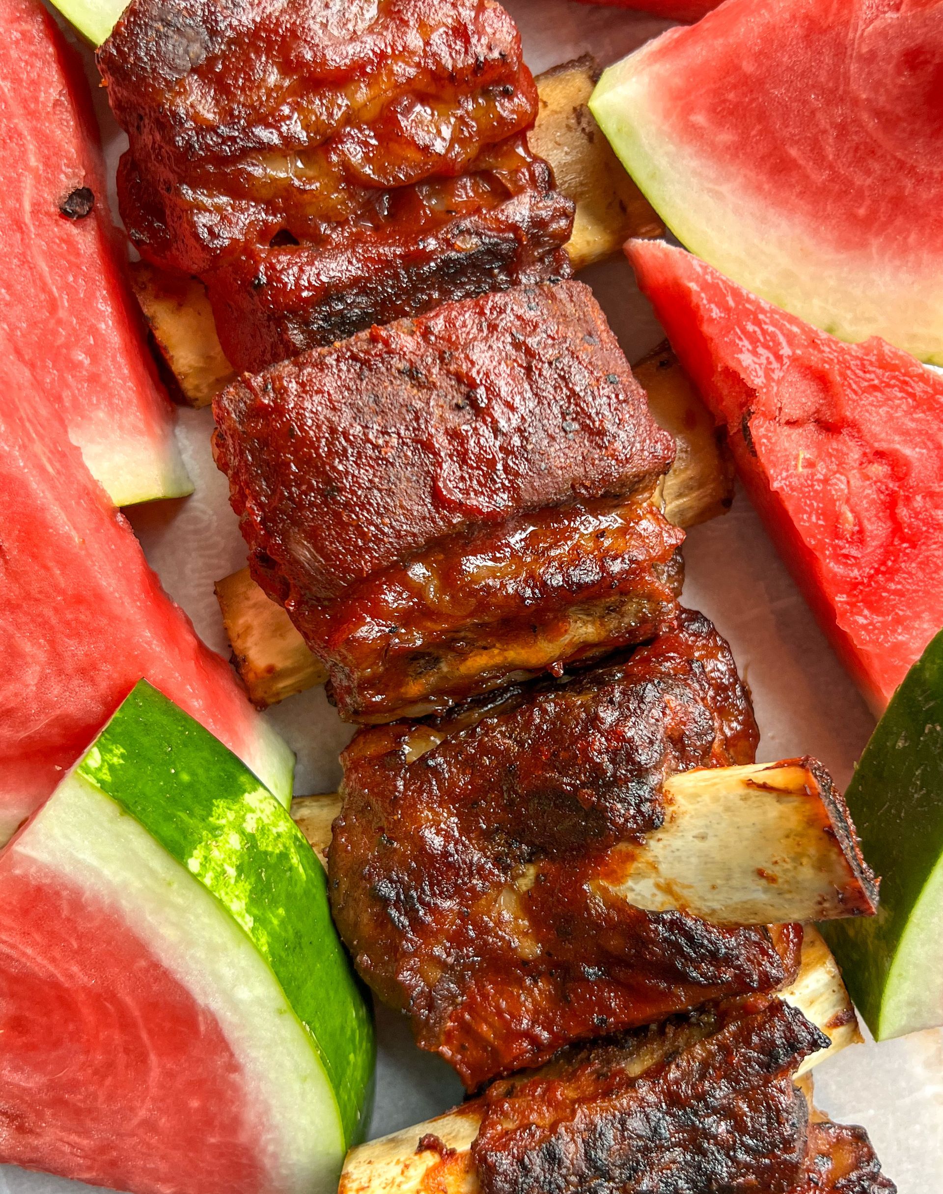 A close up of ribs and watermelon on a plate.