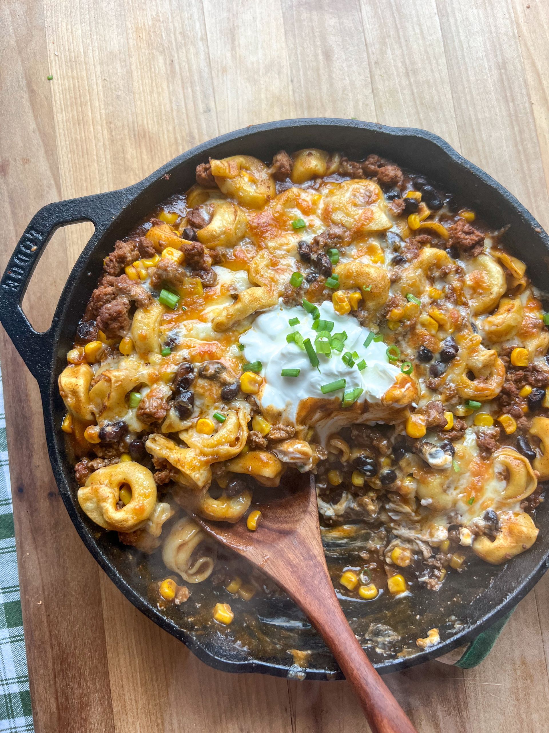 A skillet of food with a wooden spoon in it on a wooden table.