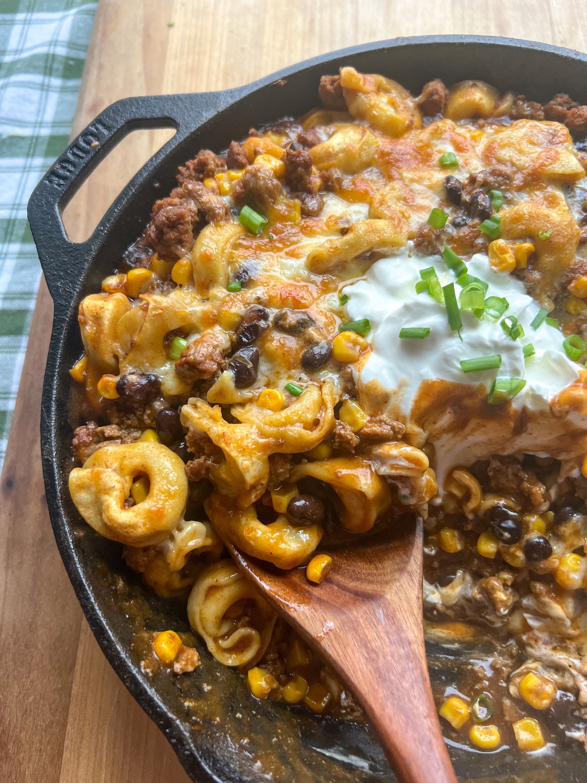 A skillet filled with macaroni and cheese with a wooden spoon in it.