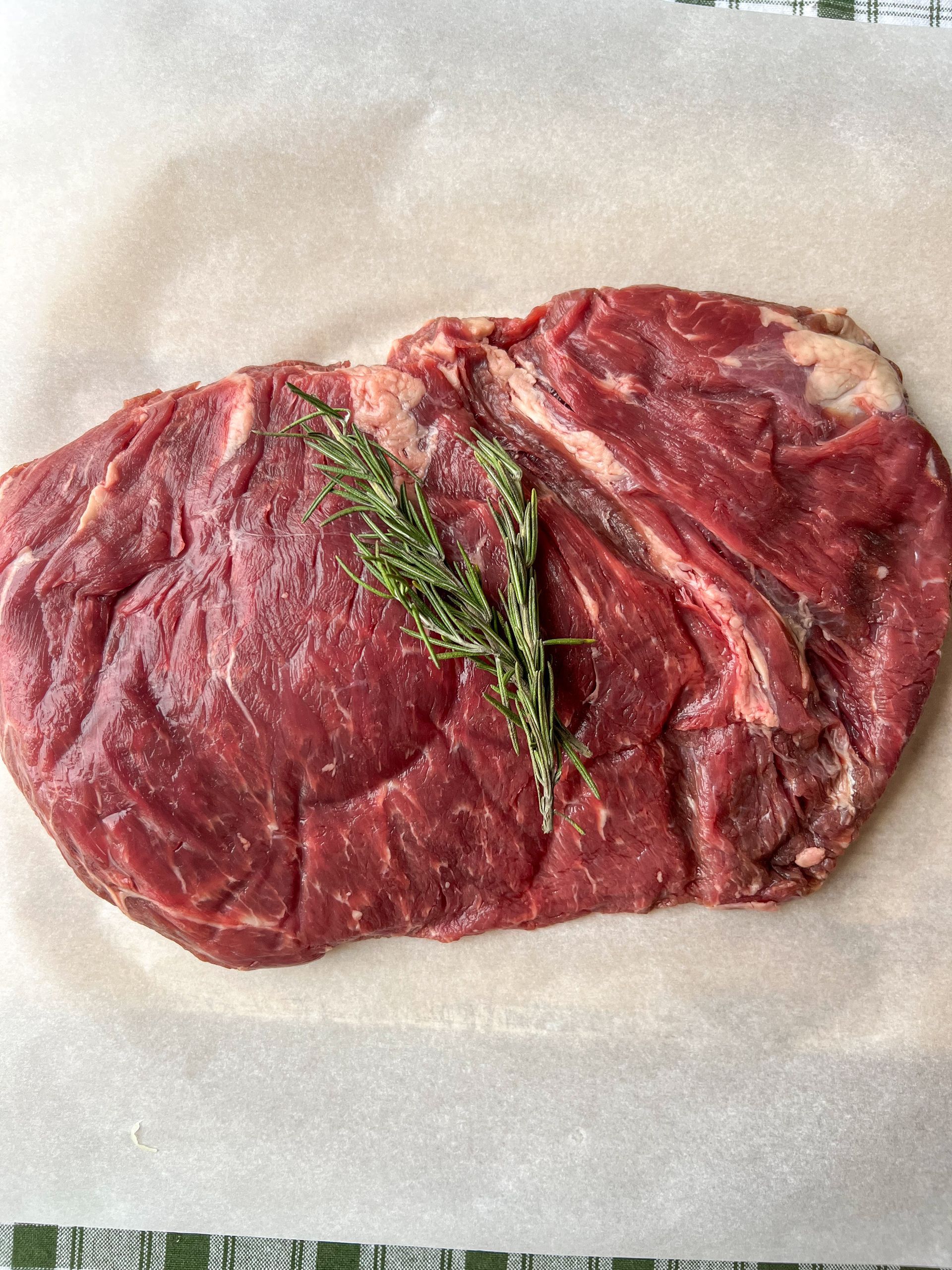 A piece of raw beef with a sprig of rosemary on a piece of wax paper.