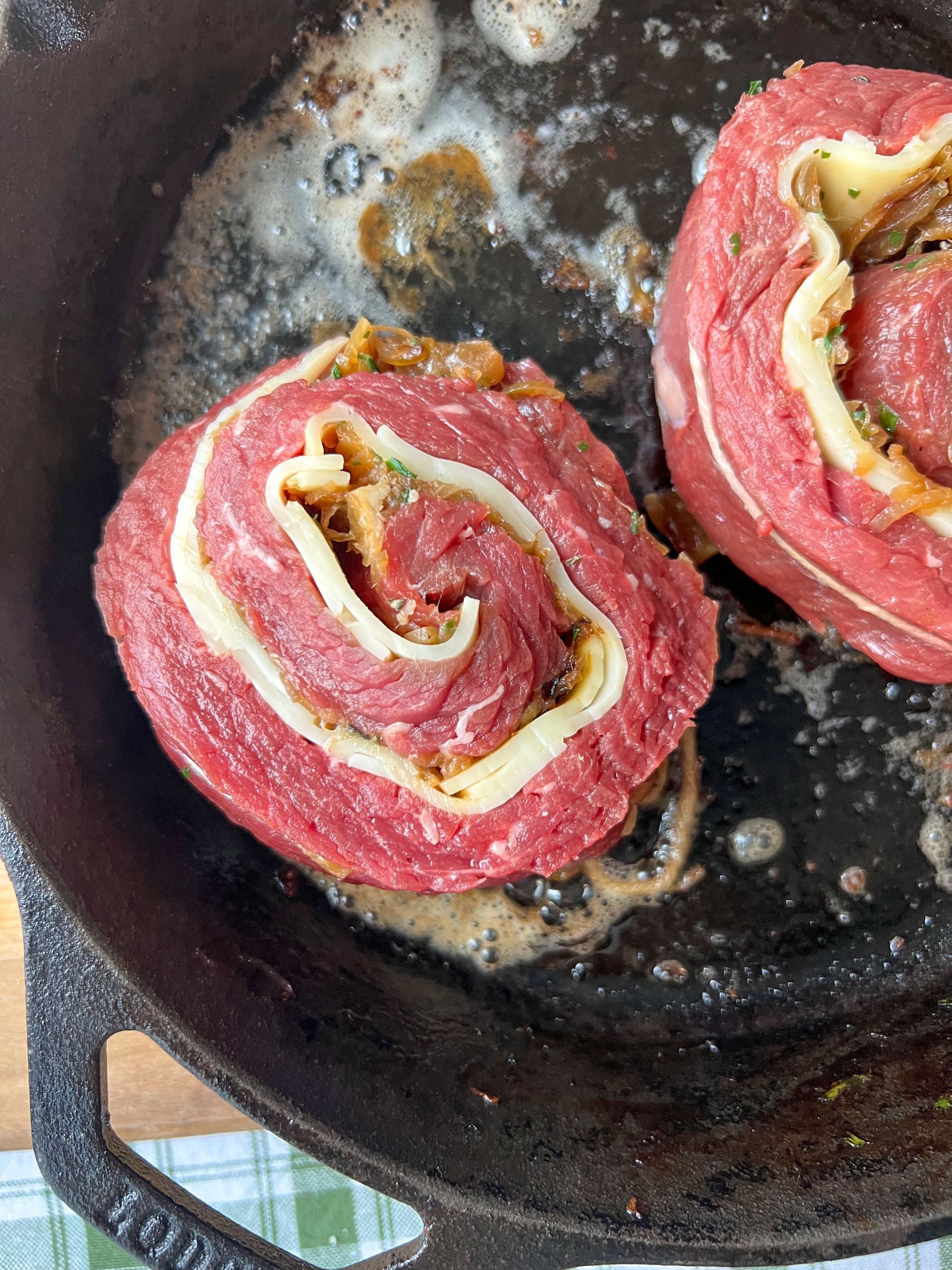 Two rolls of meat are being cooked in a skillet