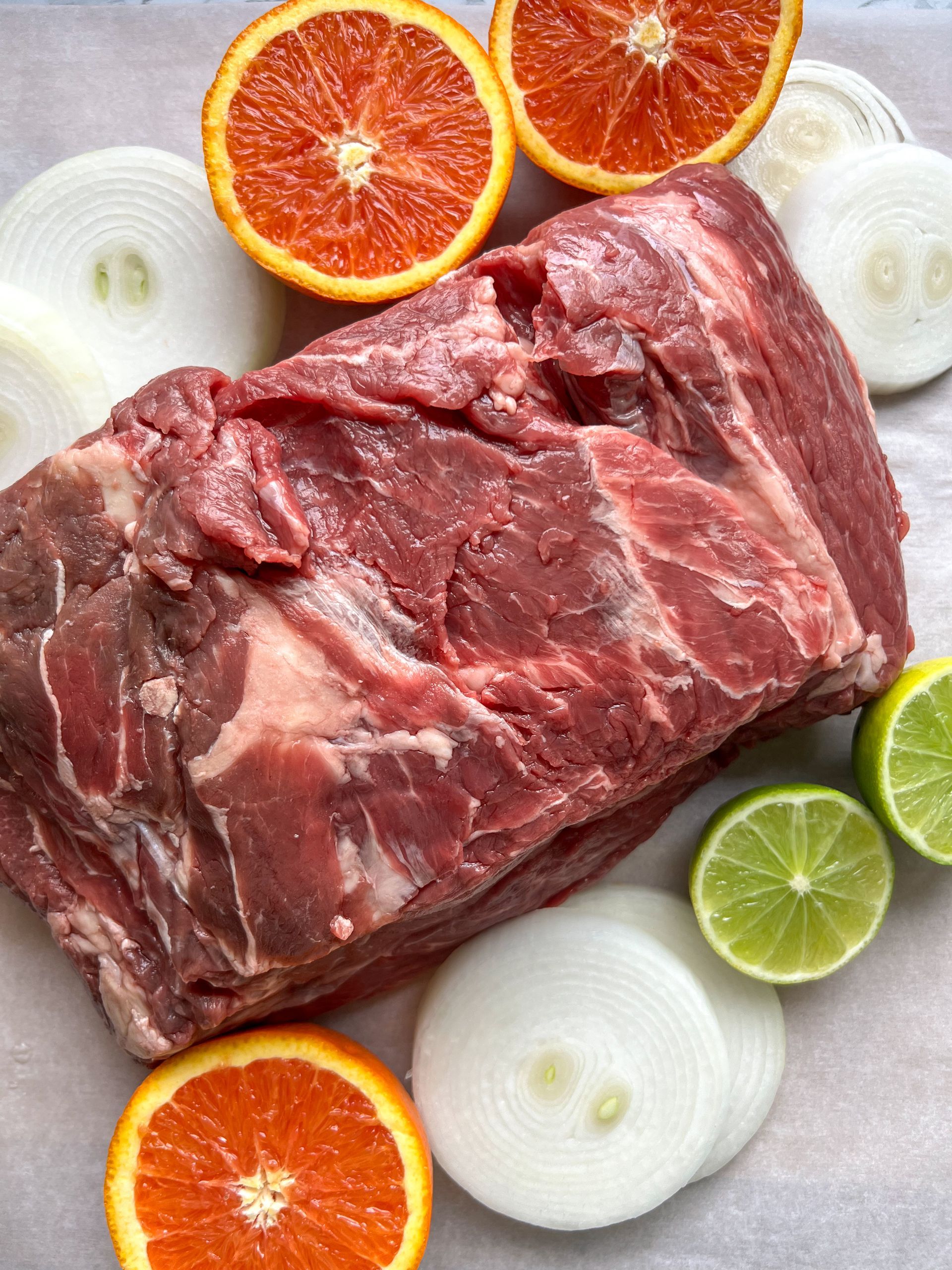 A piece of meat is surrounded by onions , oranges and limes.