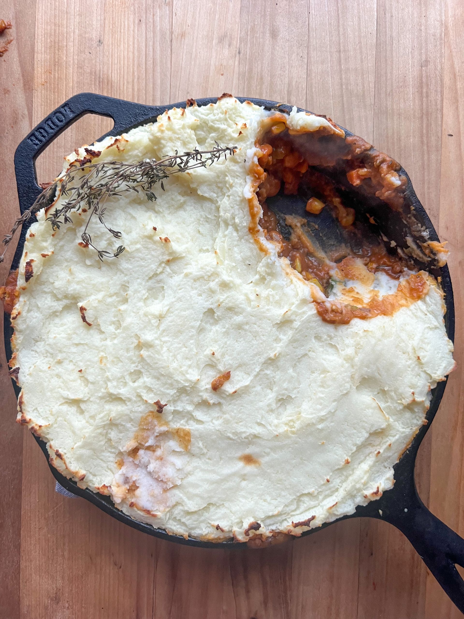 A skillet filled with mashed potatoes and meat on a wooden table.