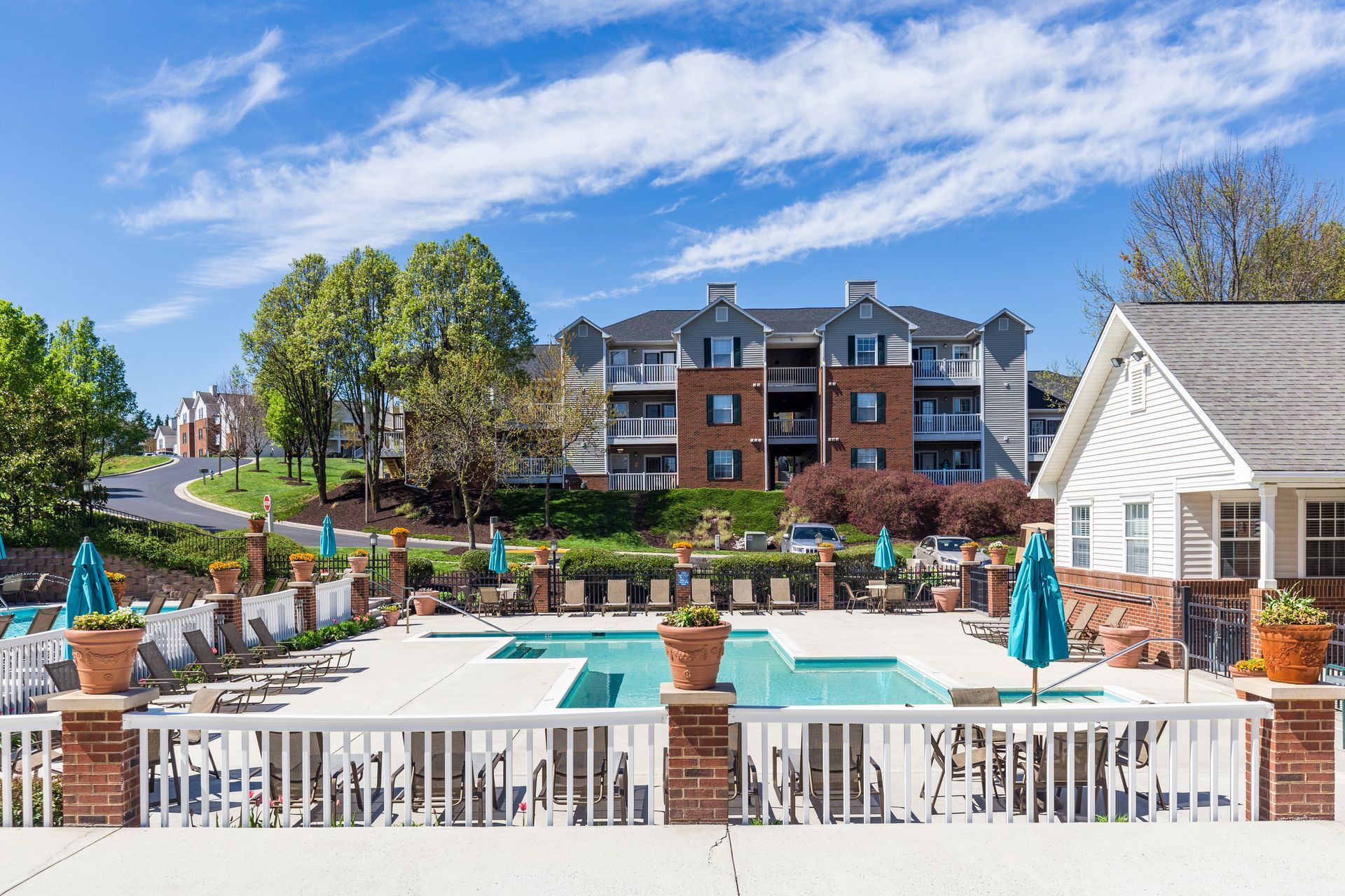 A large swimming pool surrounded by chairs and umbrellas in front of a large apartment building.