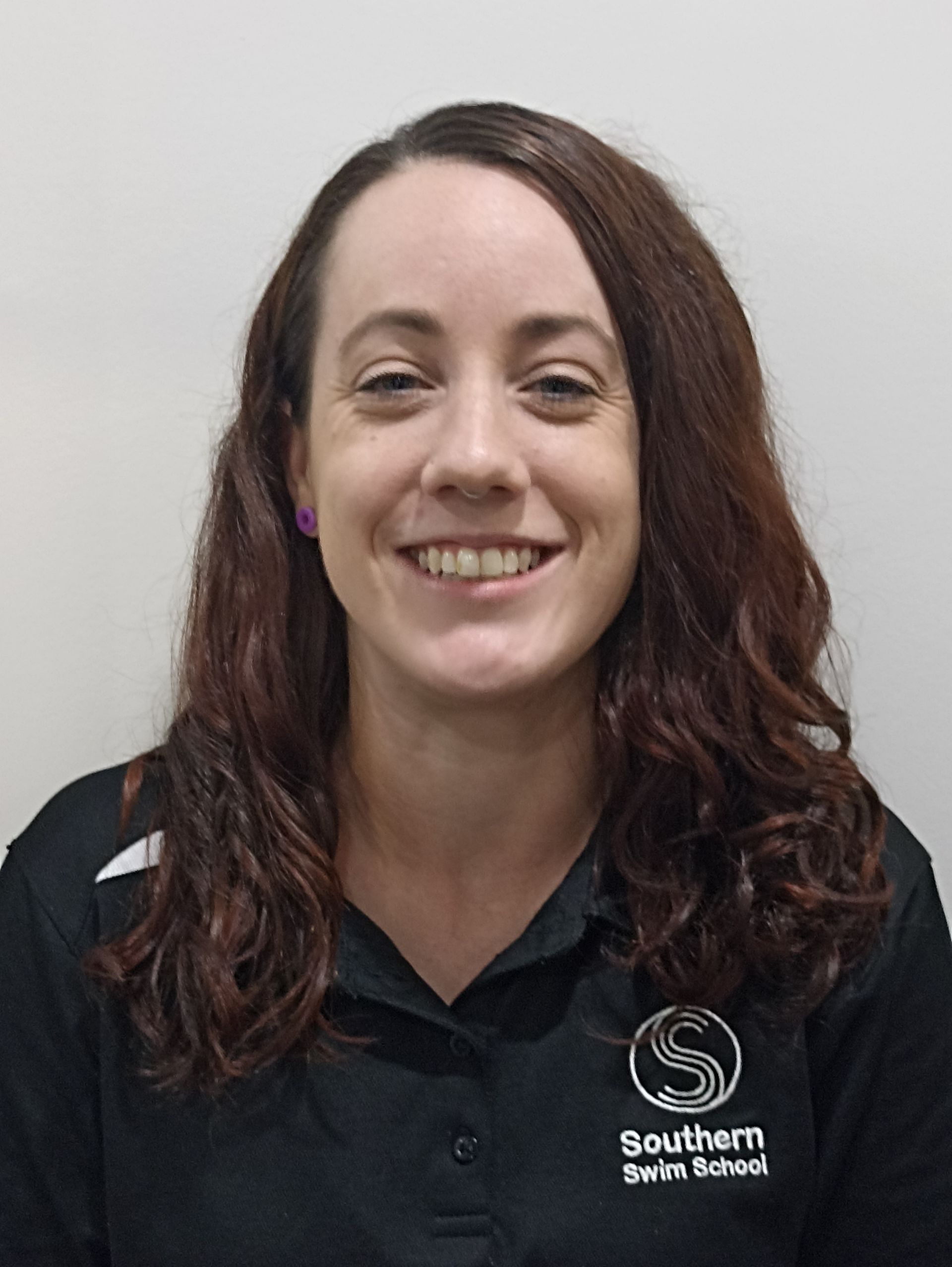 A woman with long brown hair is wearing a black shirt and smiling.