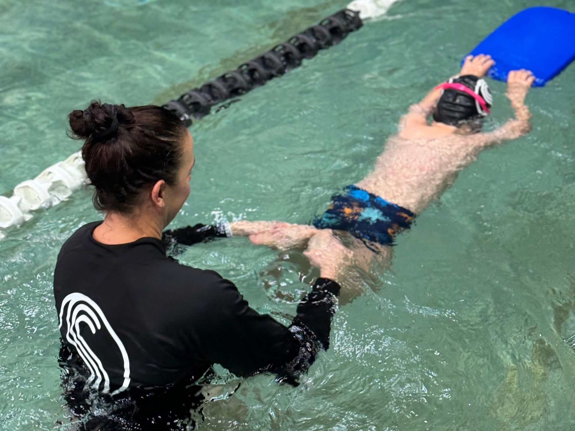A woman is teaching a young boy how to swim in a swimming pool.