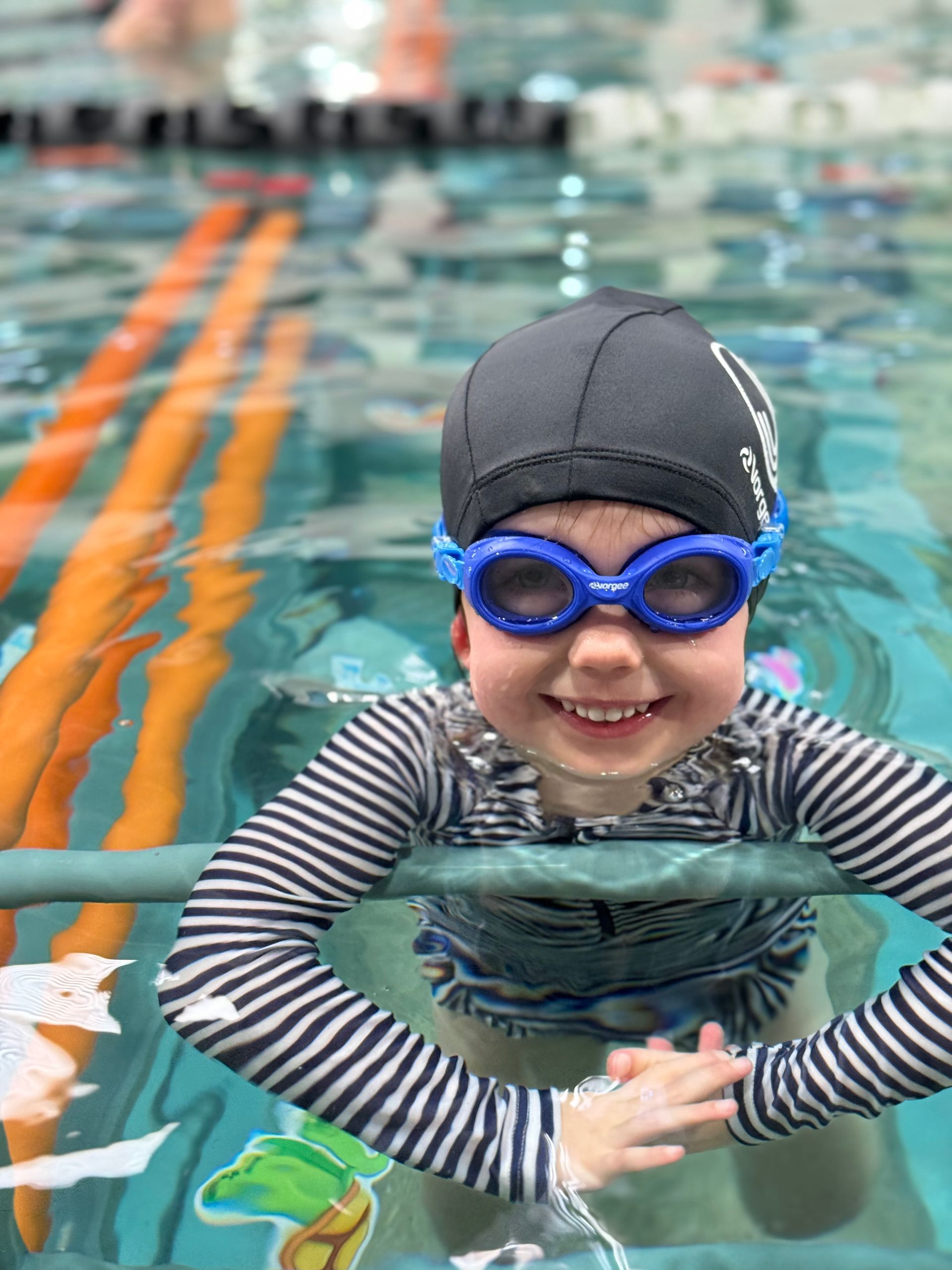 A young boy wearing goggles and a swim cap is swimming in a pool.