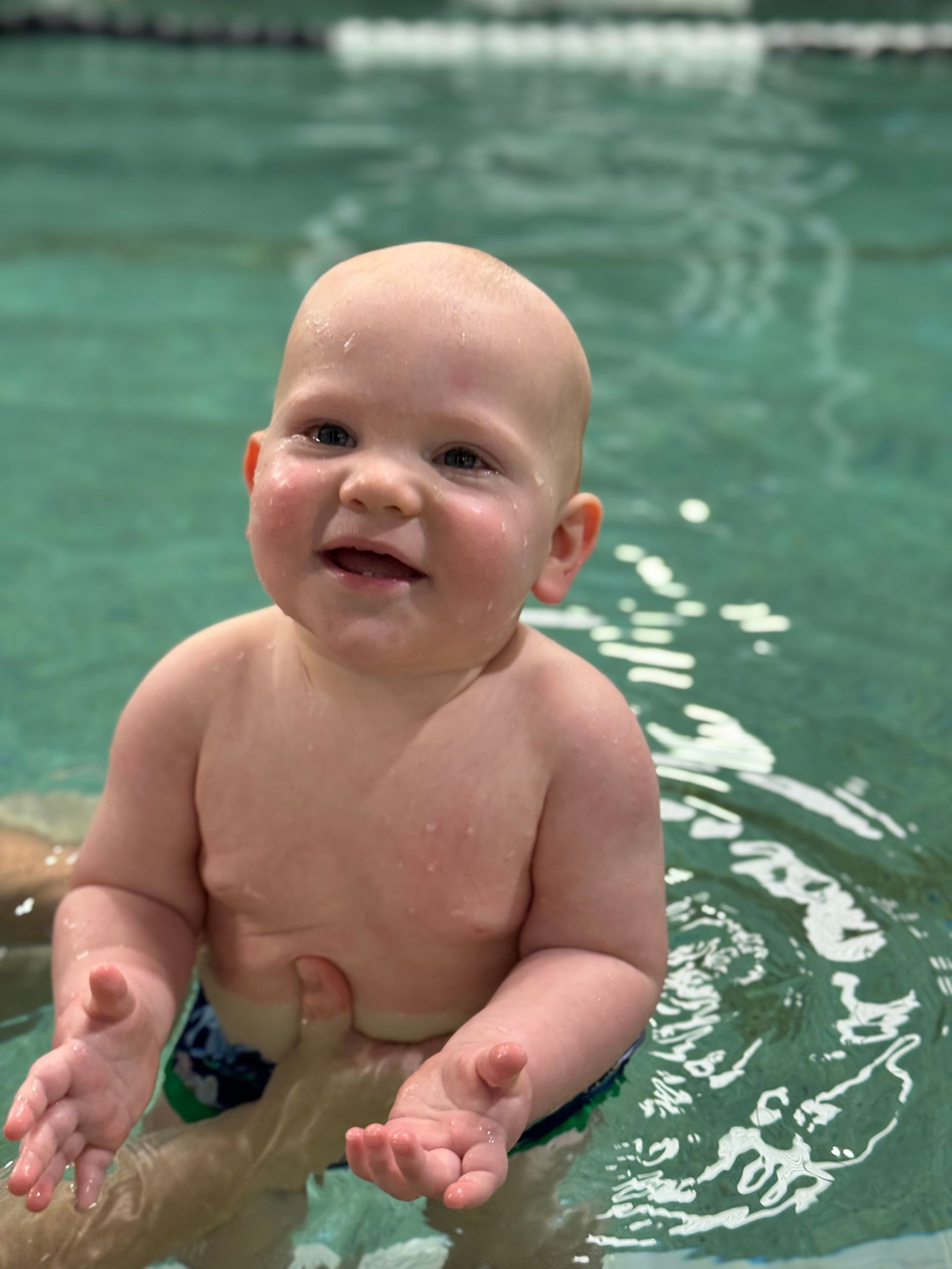 A baby is swimming in a pool and smiling at the camera.