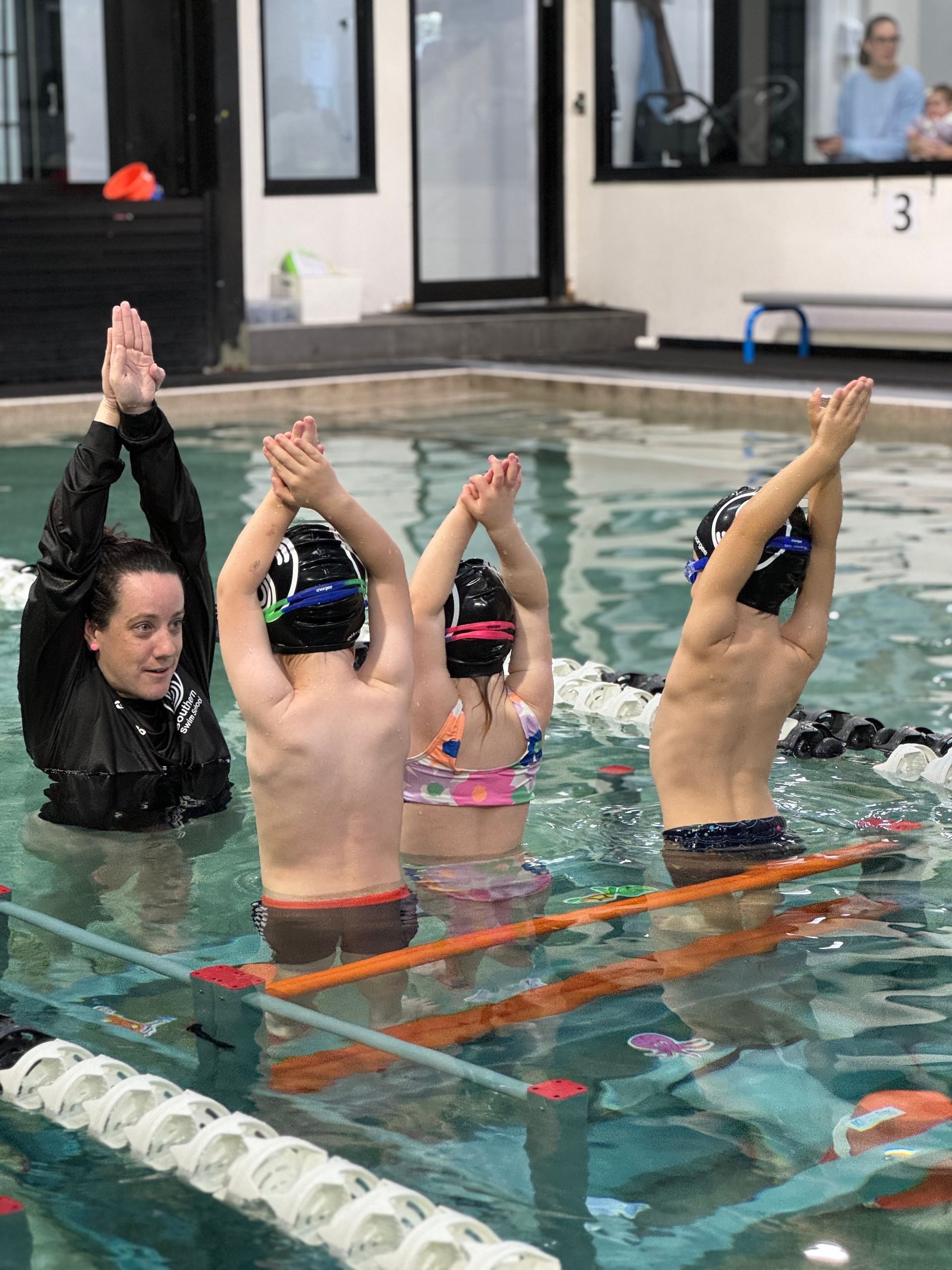 A group of children are standing in a swimming pool with their arms in the air.