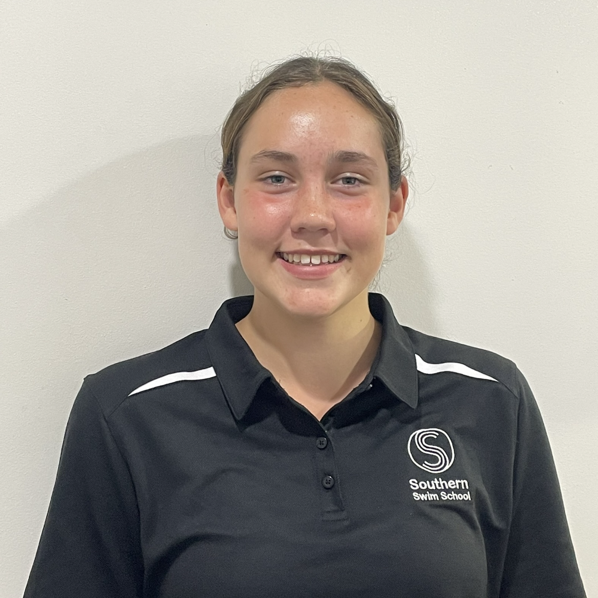 A young woman wearing a black polo shirt is smiling for the camera.