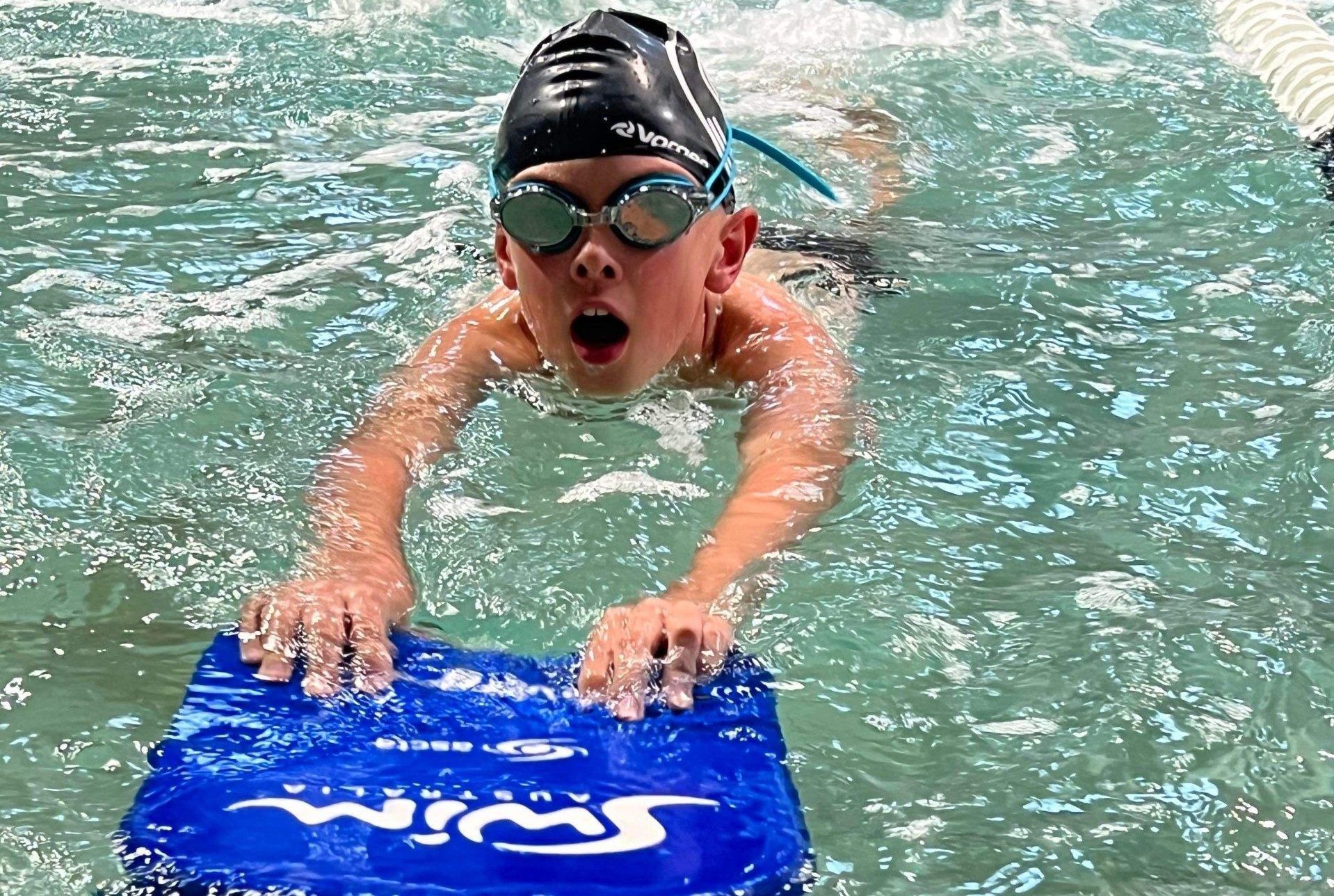 A young boy is swimming in a pool with a boogie board.