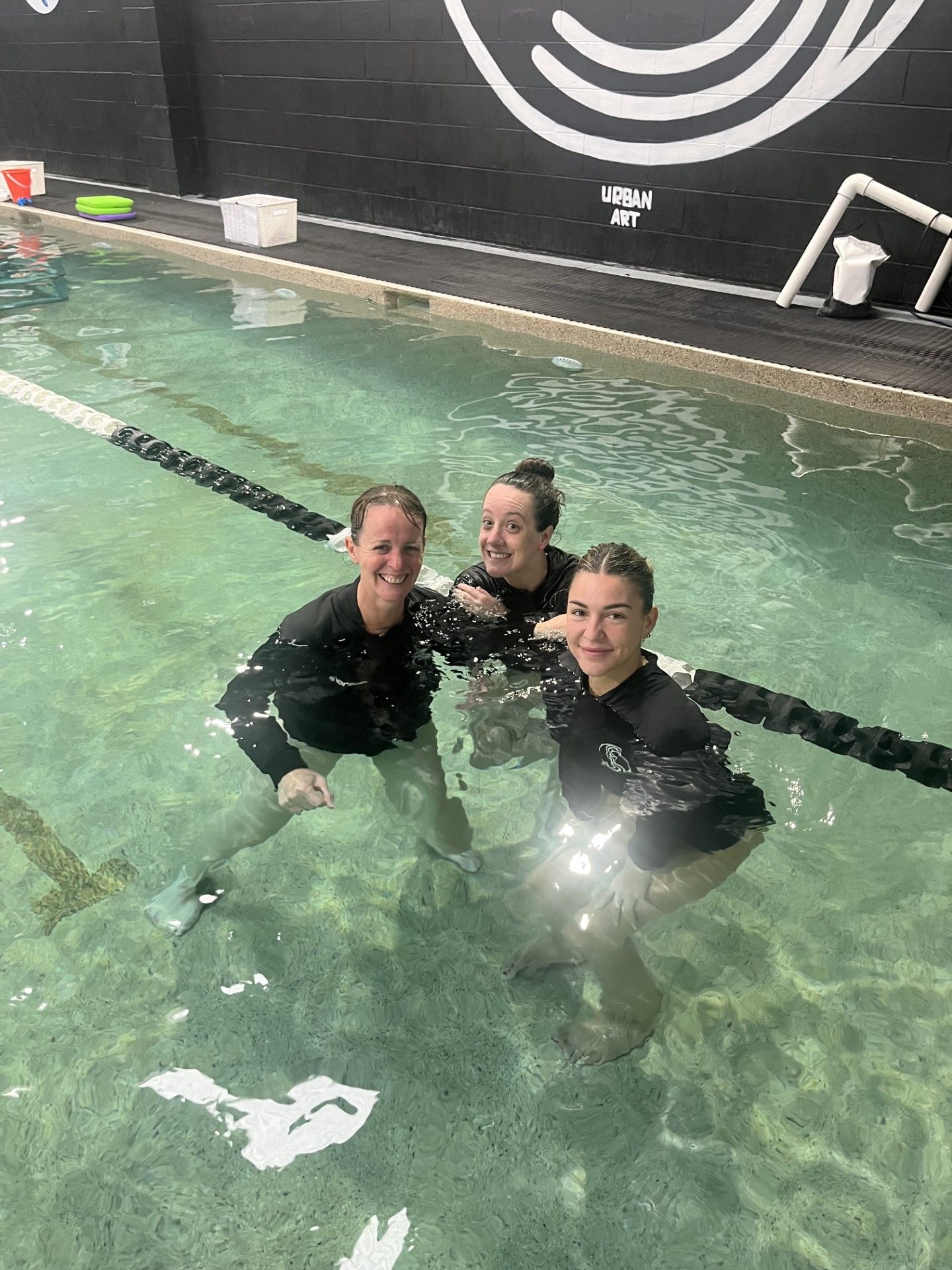 Three women are posing for a picture in a swimming pool.