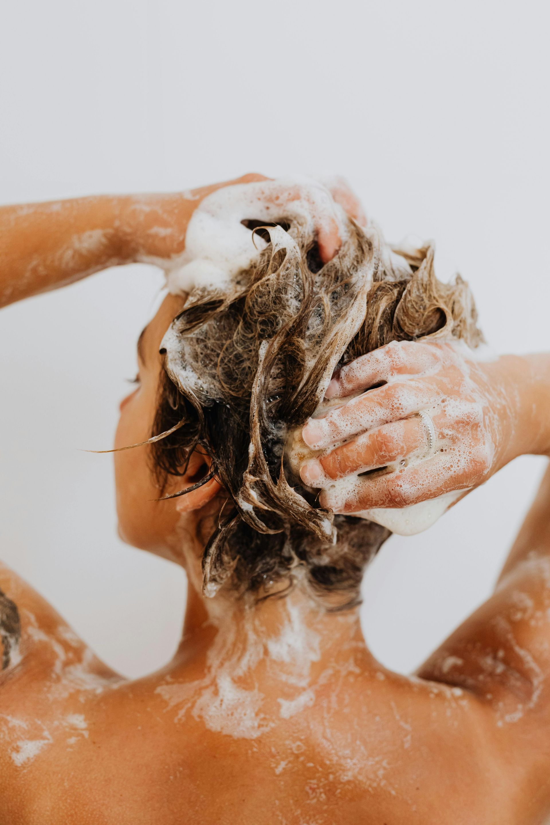Een vrouw wast haar haar onder de douche met zeep.