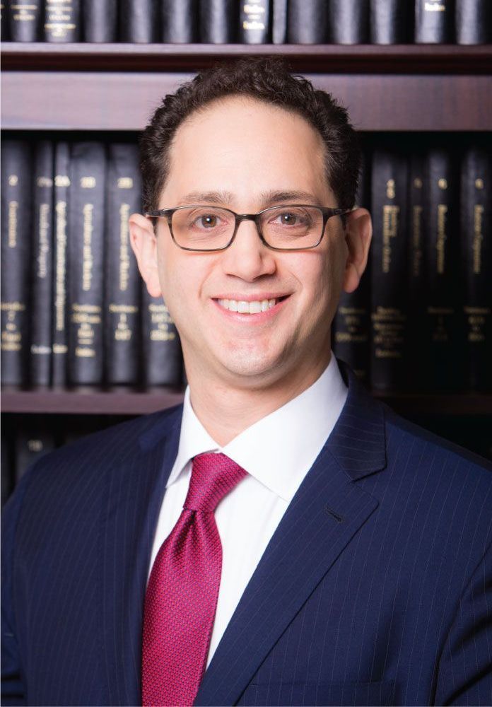 A man in a suit and tie is smiling in front of a bookshelf