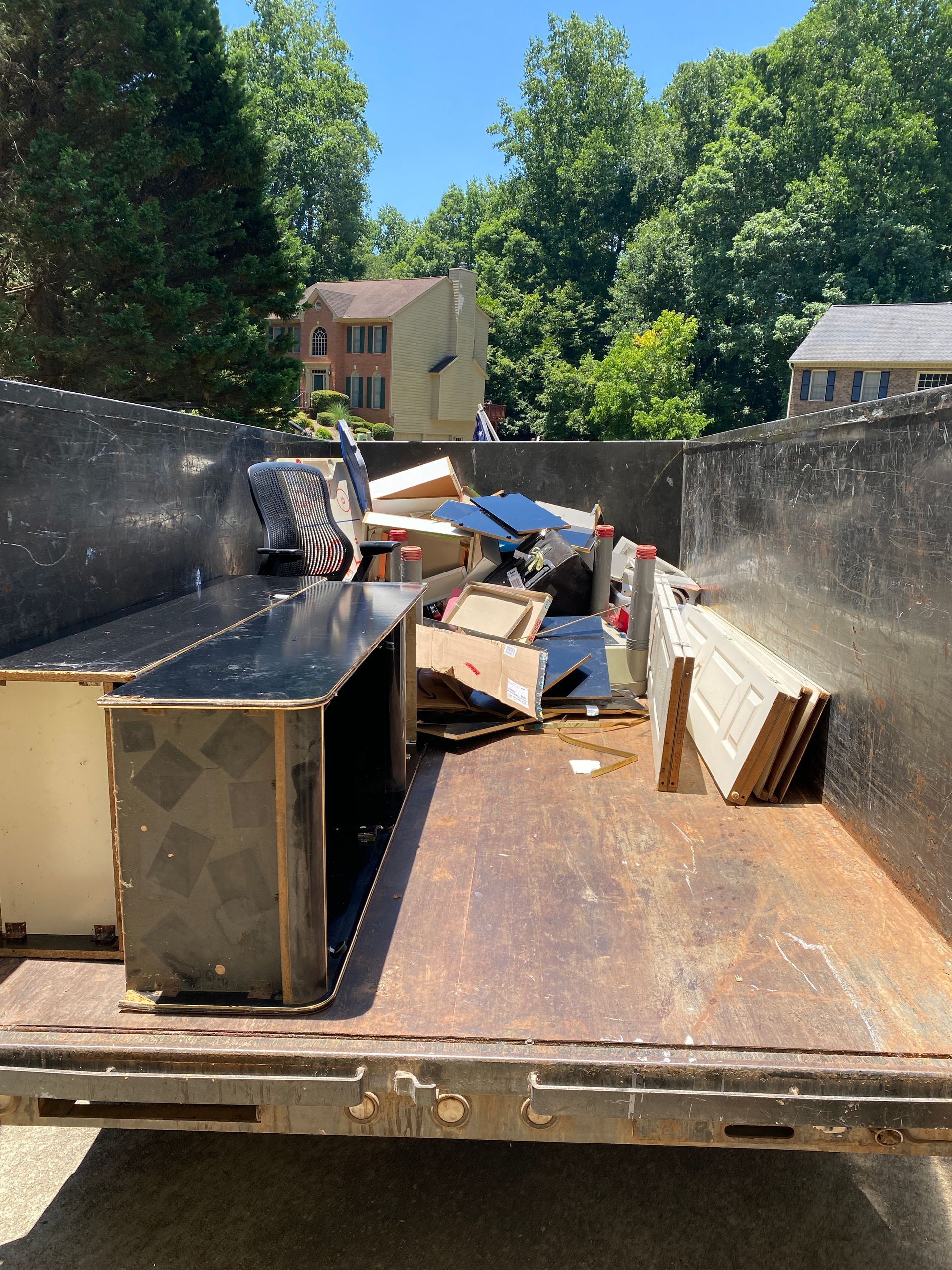 A dumpster filled with junk is parked in front of a house.