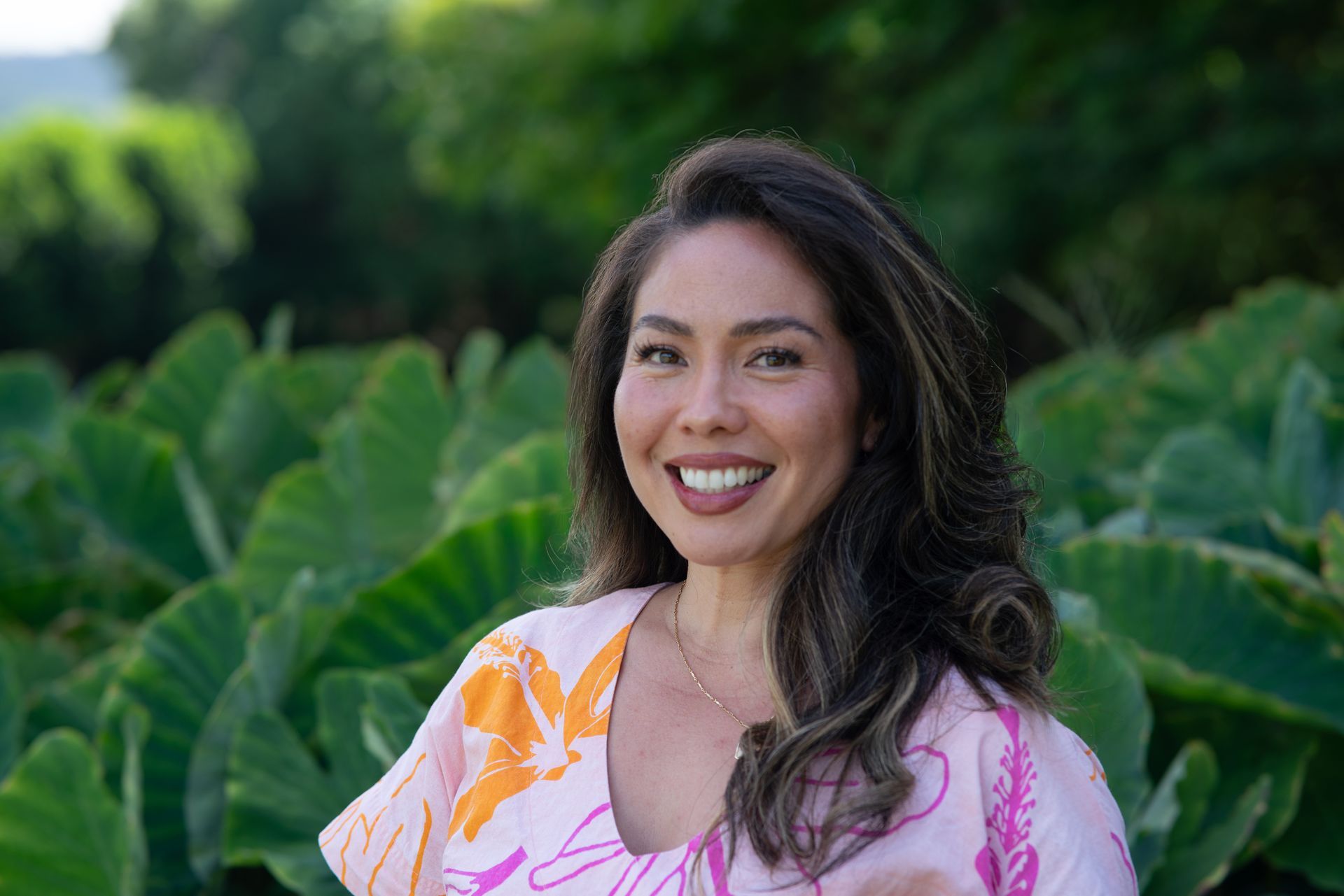 Smiling woman in a pink floral top standing in front of large green leaves outdoors Smiling woman in a pink floral top standing in front of large green leaves outdoors