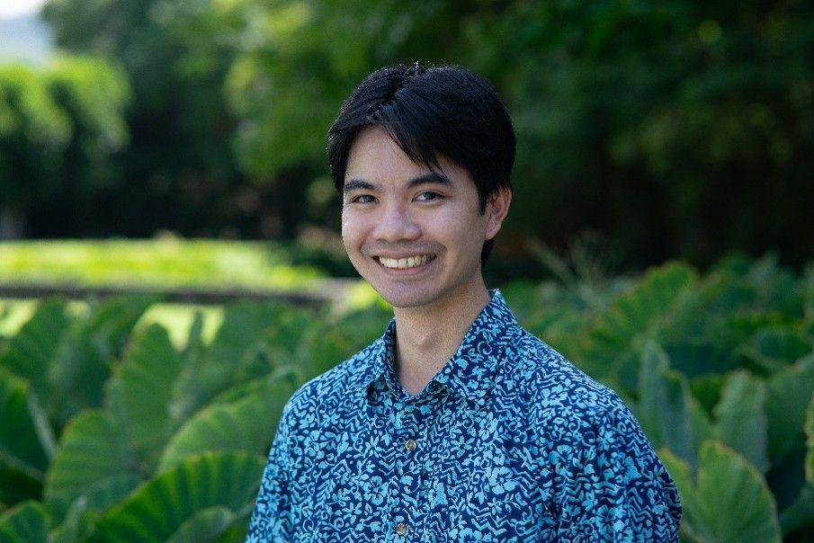 Smiling person in a blue patterned shirt standing in a lush green garden Smiling person in a blue patterned shirt standing in a lush green garden