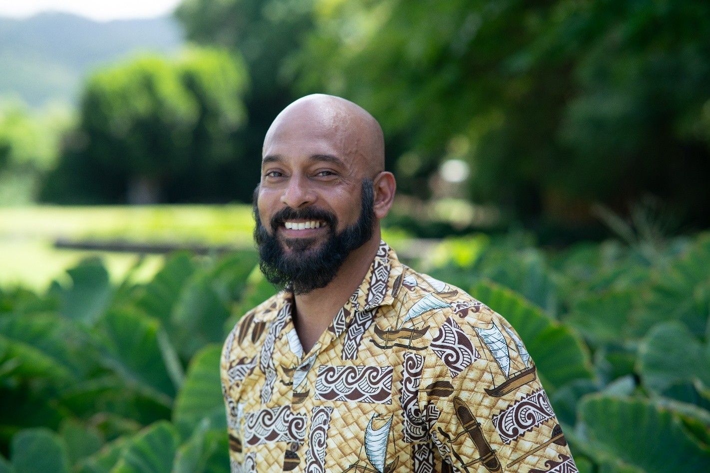 Smiling man in a yellow patterned shirt standing outdoors in a lush green garden Smiling man in a yellow patterned shirt standing outdoors in a lush green garden