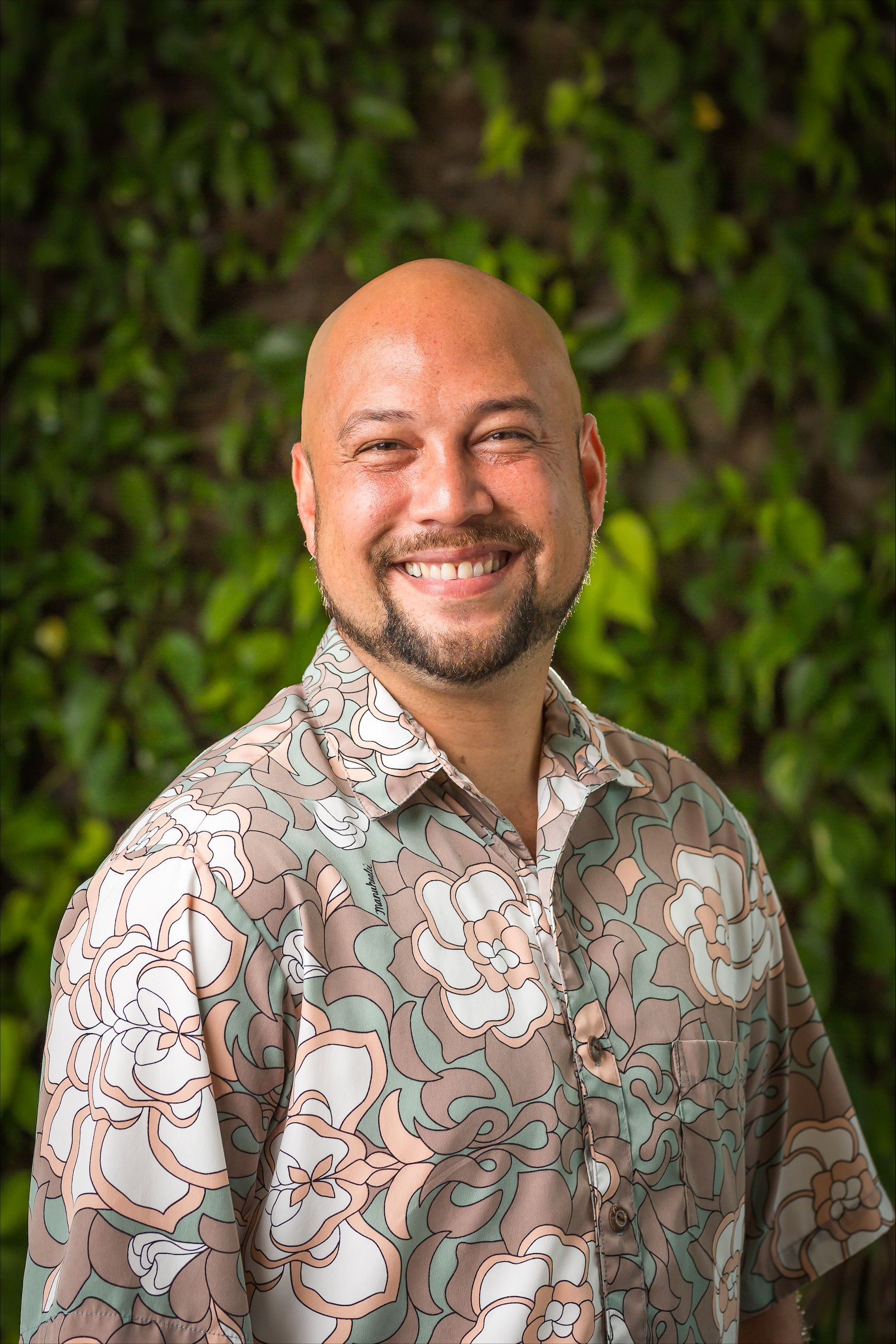 Smiling man in a patterned shirt standing before a leafy green background Smiling man in a patterned shirt standing before a leafy green background