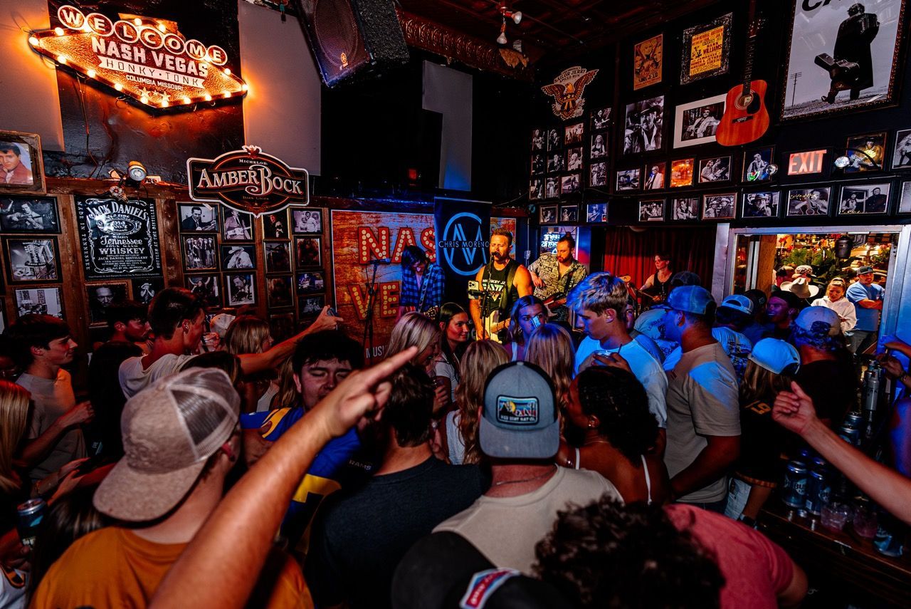 Crowded bar concert with people raising hands under blue and orange lights and posters on the walls