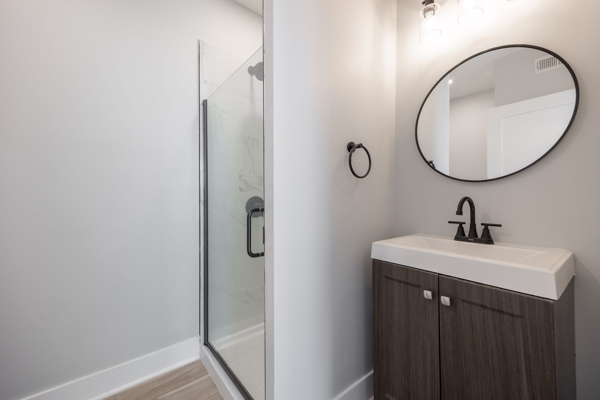 Modern bathroom with glass shower, round mirror, and dark wood vanity with black faucet.