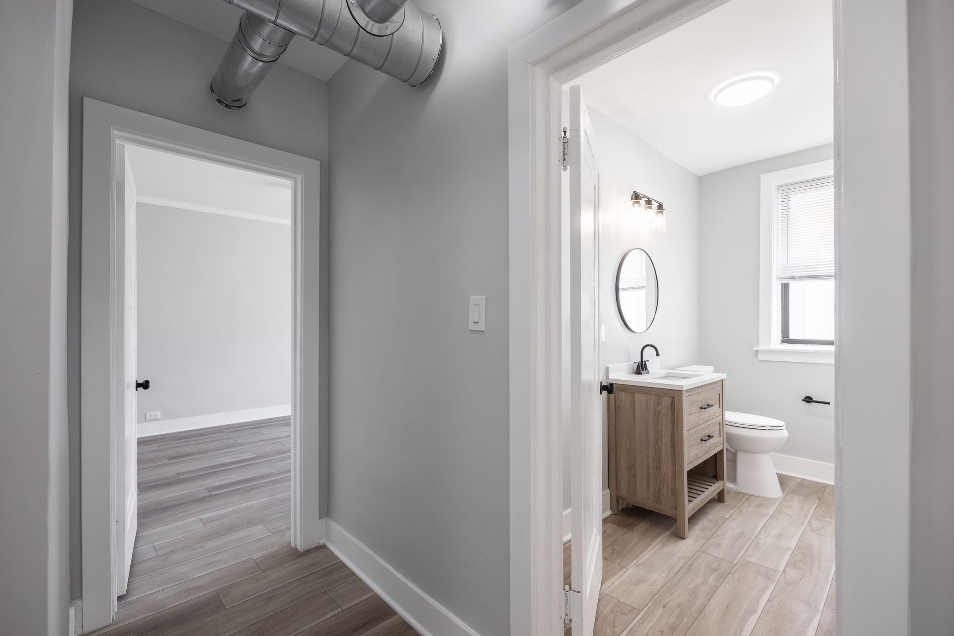 Hallway with open doors to a bedroom and a bright bathroom with vanity and toilet