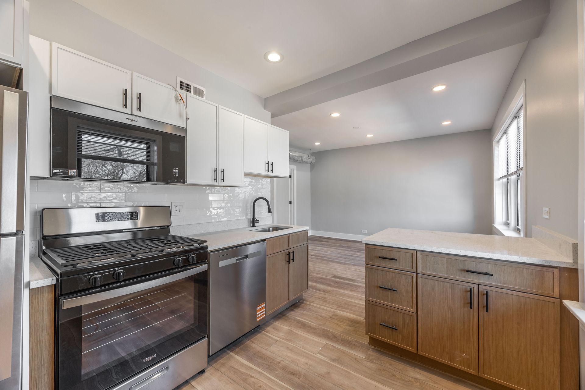 Modern kitchen with white cabinets, stainless appliances, and a long windowed countertop.