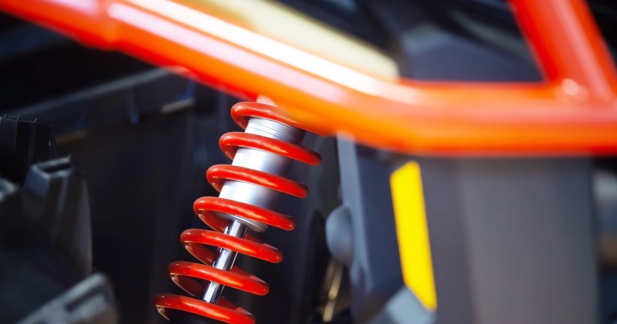 A close-up of a bright red coil spring shock absorber attached to an orange tubular frame on a vehicle.