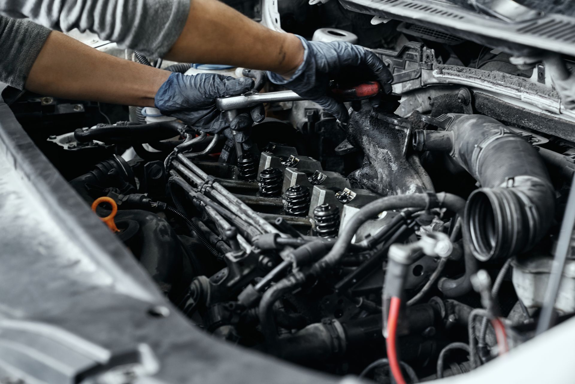 A person wearing gloves uses a wrench to work on the engine of an open-hood vehicle.