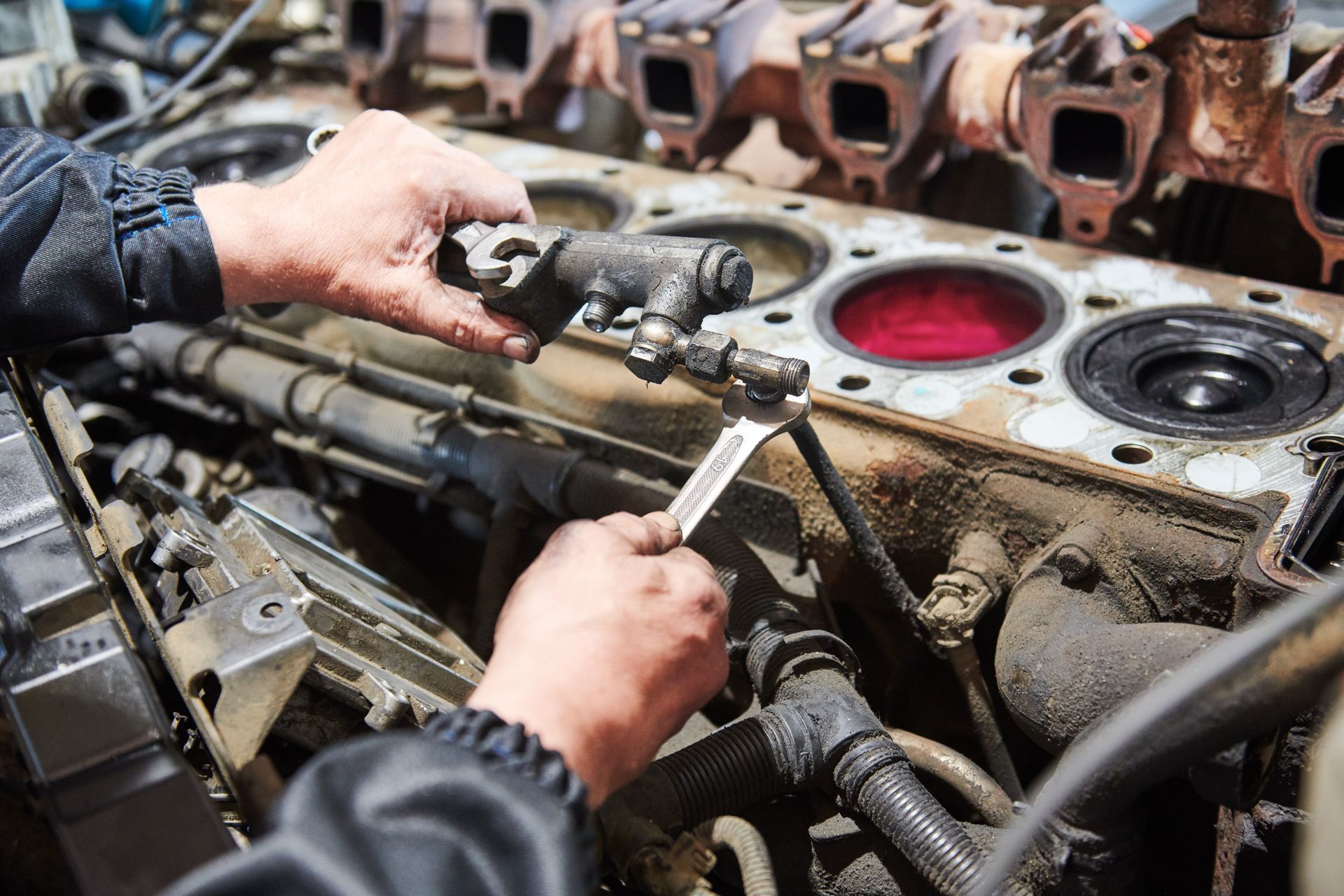 Hands using a wrench to repair a disassembled engine, showing internal mechanical components.