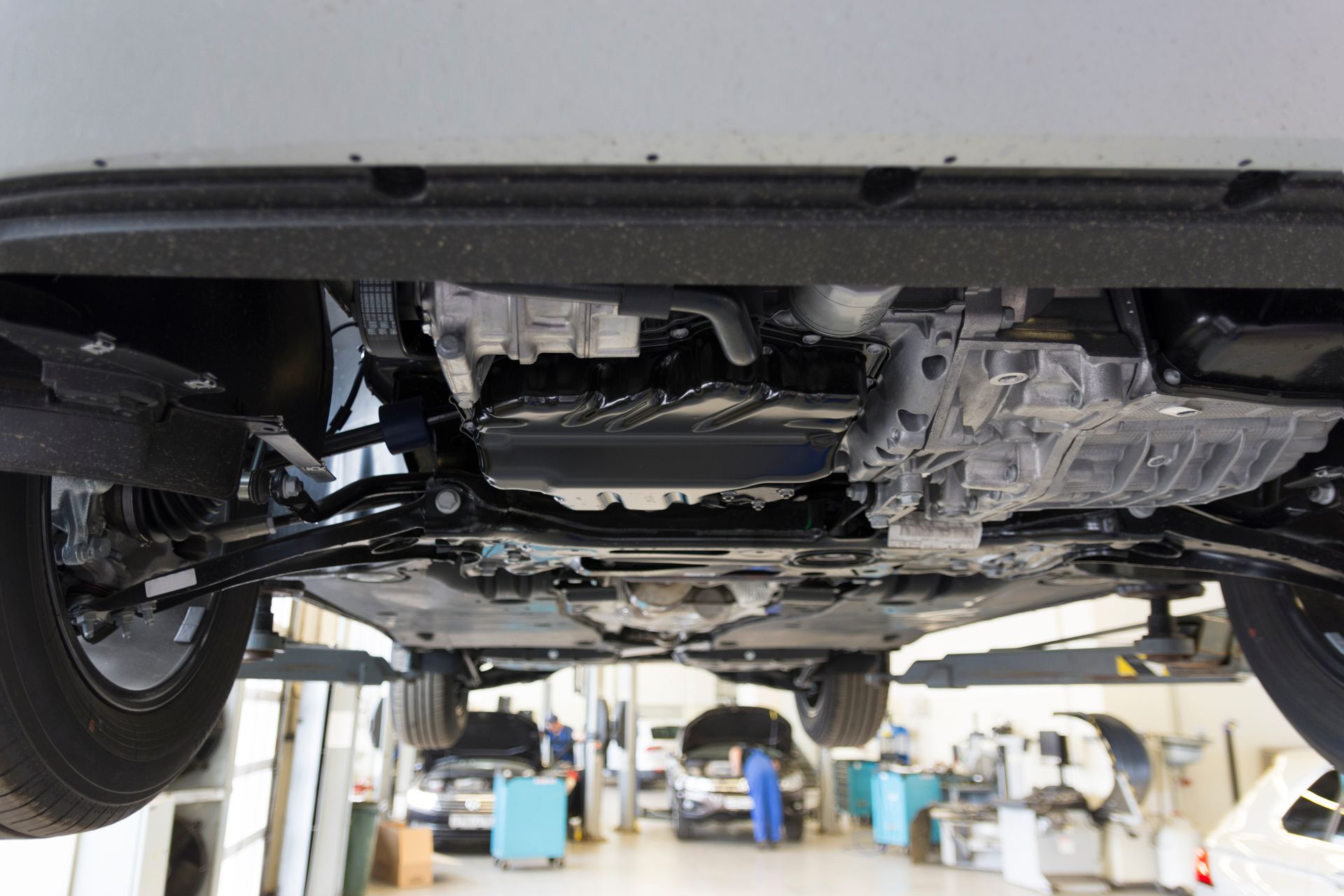 The underside of a car raised on a lift in a brightly lit automotive repair shop.