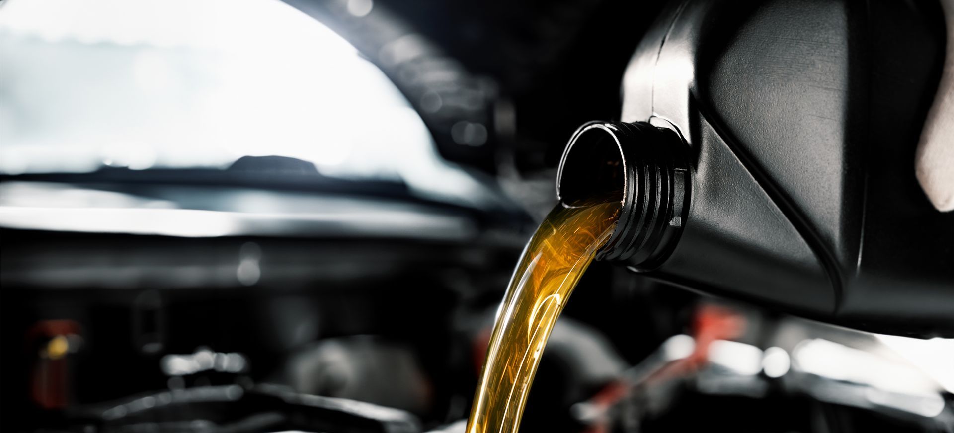 Golden motor oil pouring from a plastic container into a car engine.