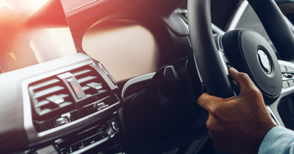 A person's hand on a car steering wheel inside a modern vehicle interior.