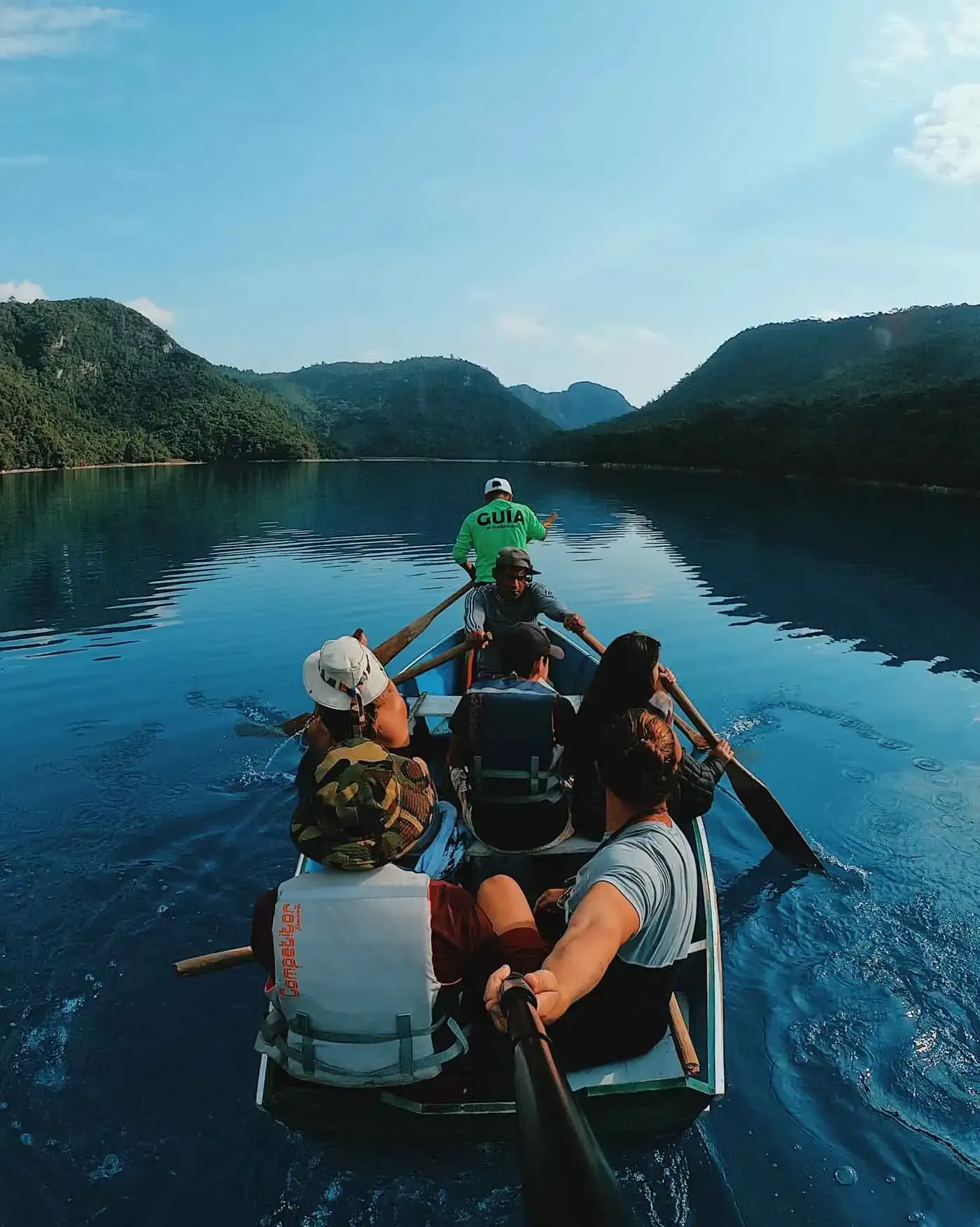 People paddling a canoe on a calm blue lake surrounded by forested mountains