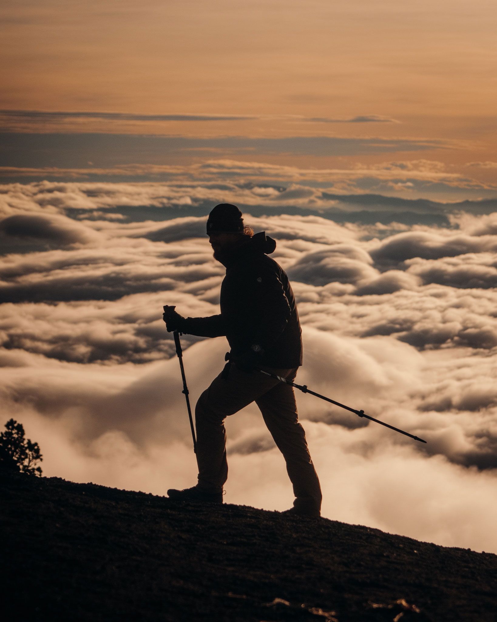 Silhouette of a hiker on a mountain ridge above a sea of clouds at sunrise