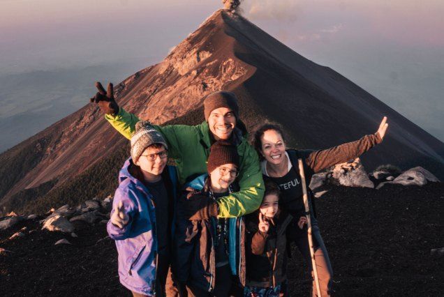 Four friends smiling with arms raised on a volcanic ridge at sunset