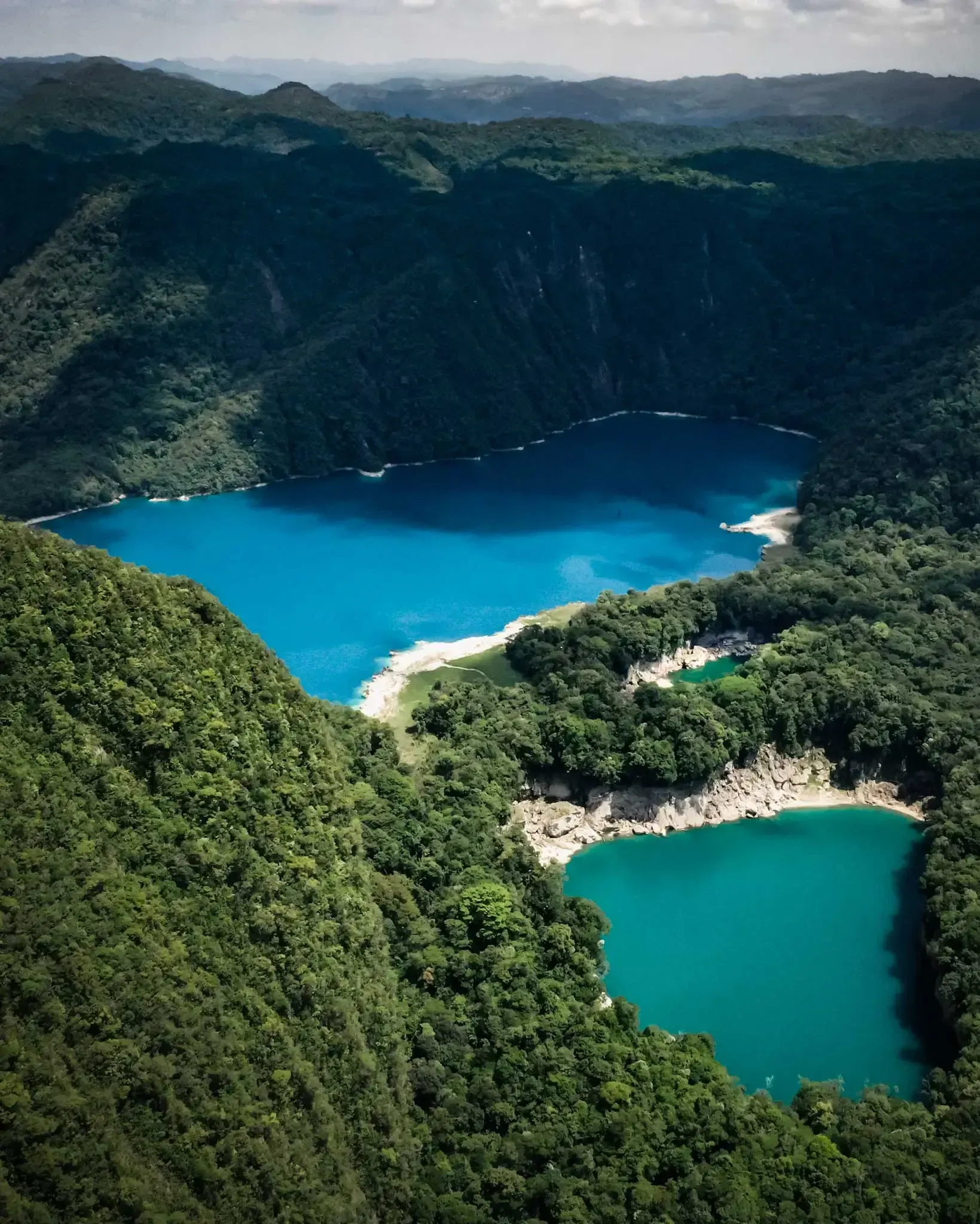 Aerial view of turquoise lagoons surrounded by lush green mountains and forest