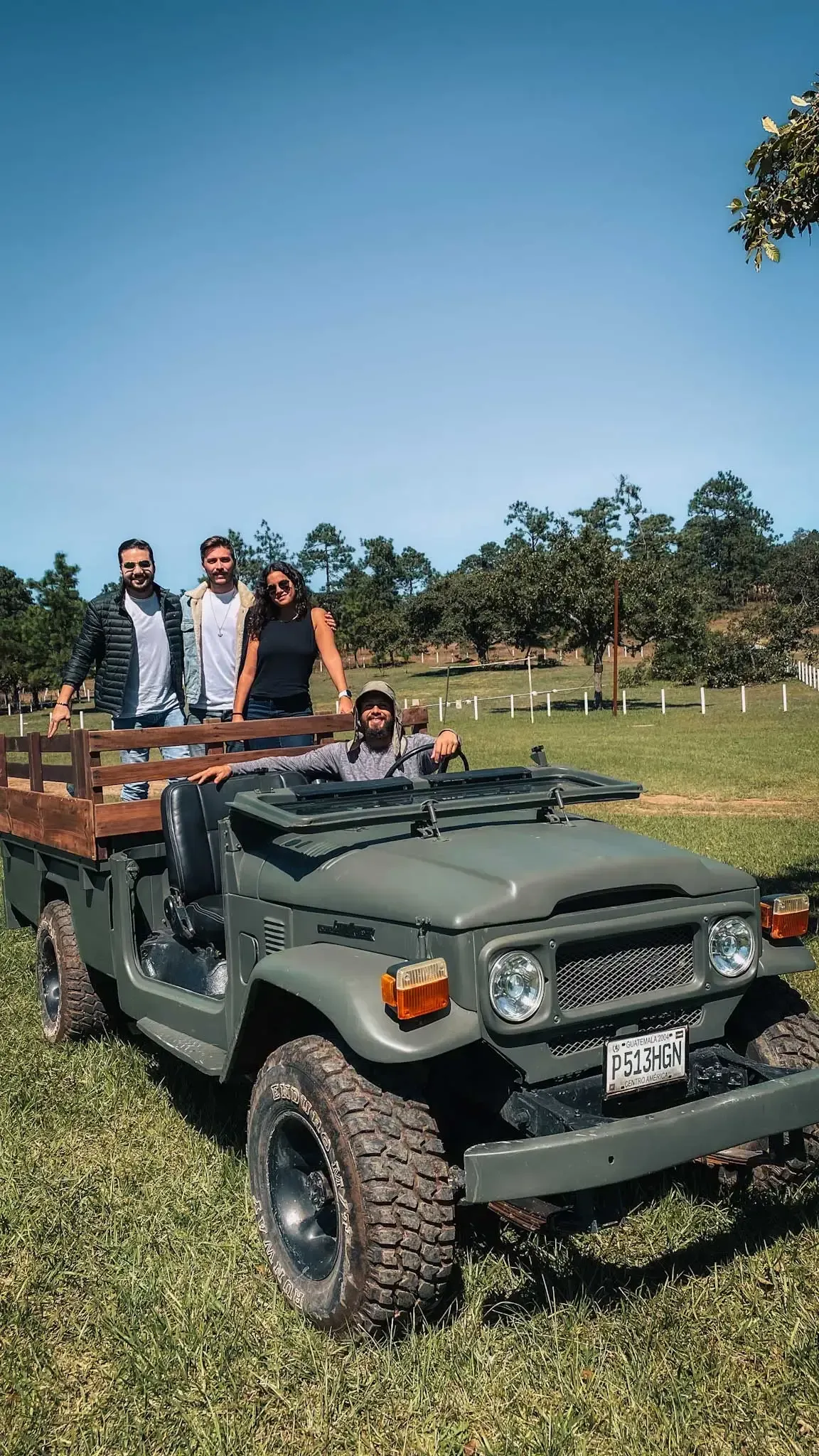 People standing on a green off-road vehicle in a grassy field under a clear blue sky.