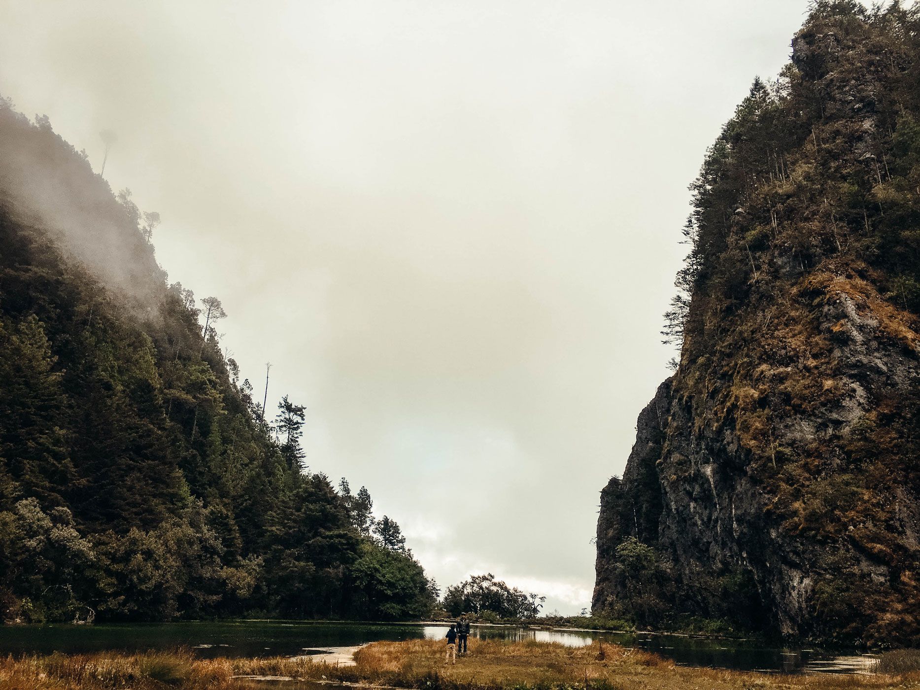 Misty river canyon with steep dark cliffs and a small boat near the water