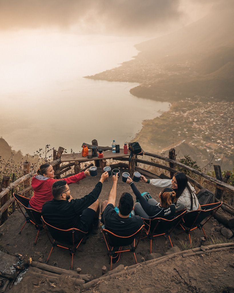 People seated on a cliff overlook, looking out over a hazy coastline and bay at sunset.